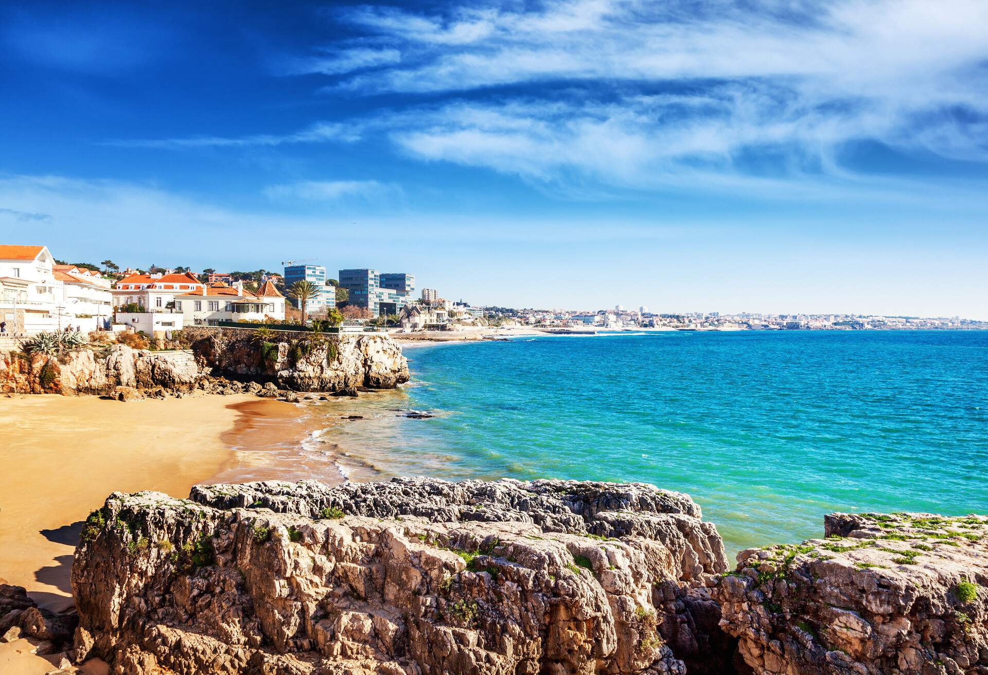 A beach with gentle waves and rocky coastlines along a coastal city.