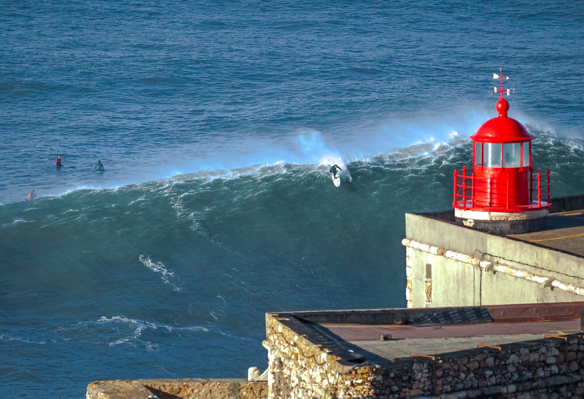 A red lighthouse overlooking the ocean with surfers riding the waves.