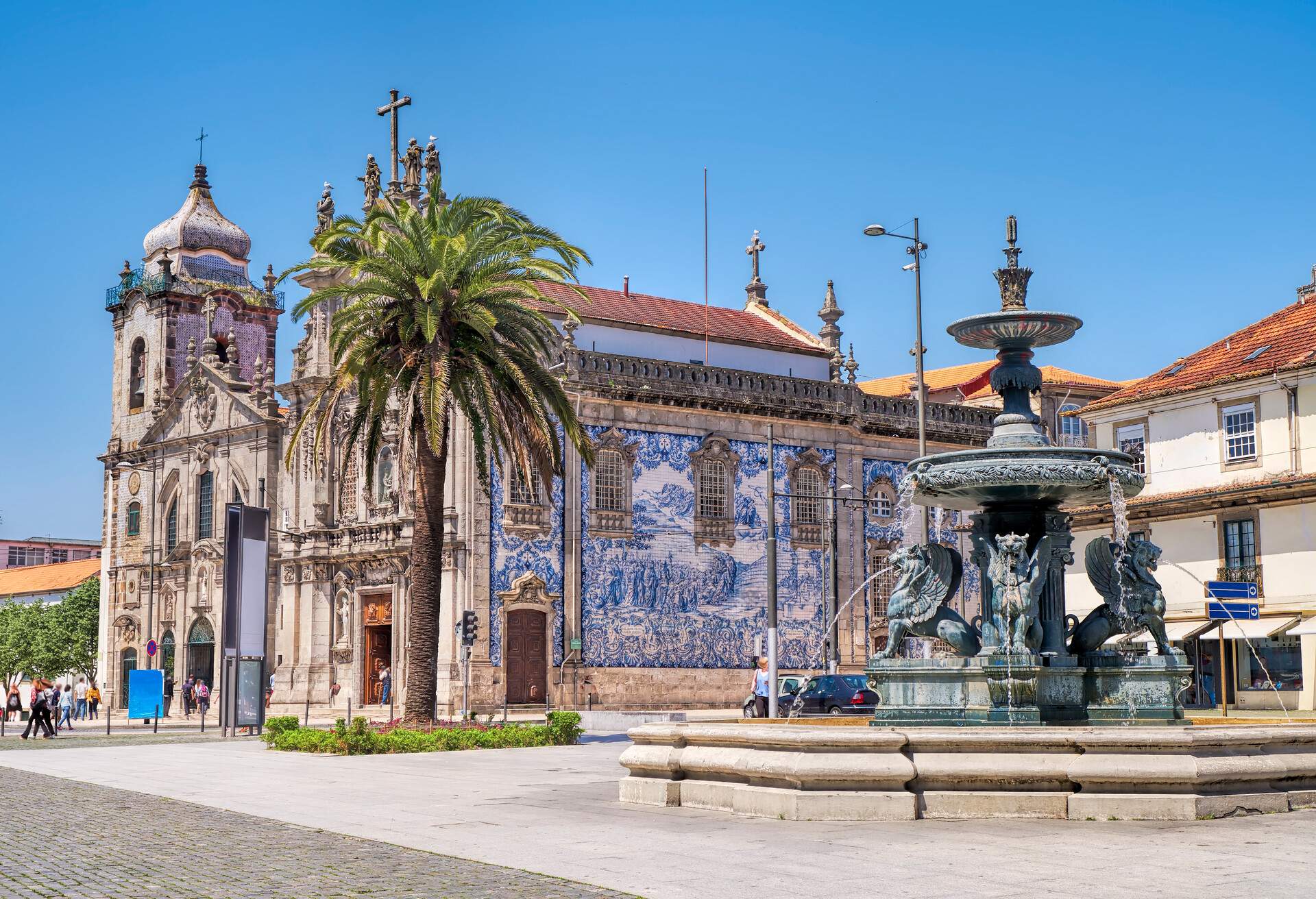 An ancient water fountain next to a historic church with an azulejo-decorated side wall. 