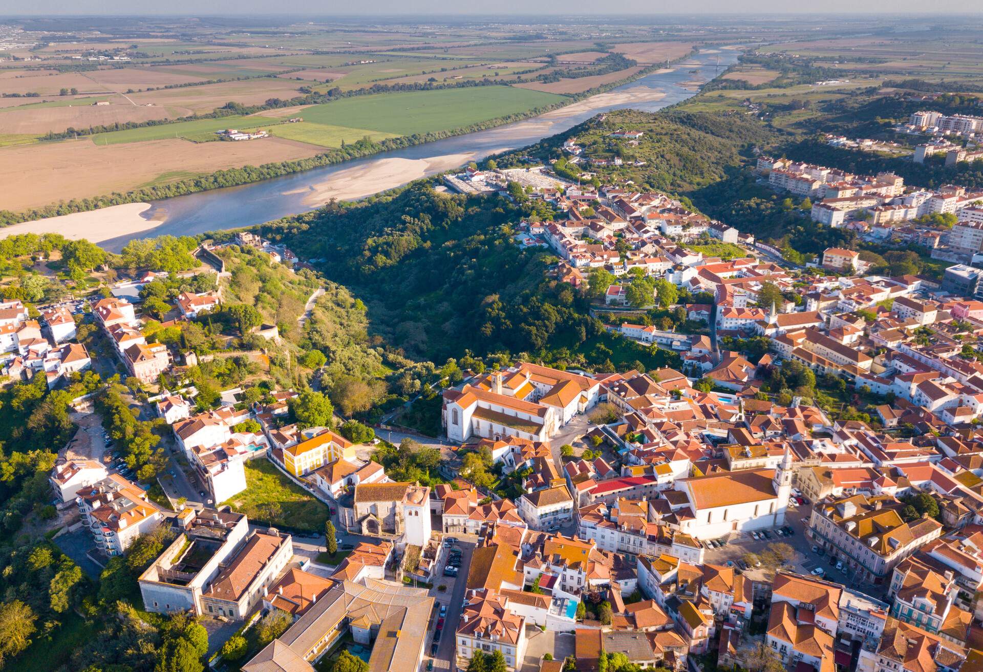 Numerous houses nestled on one side of the river, while a lush field is on the opposite.