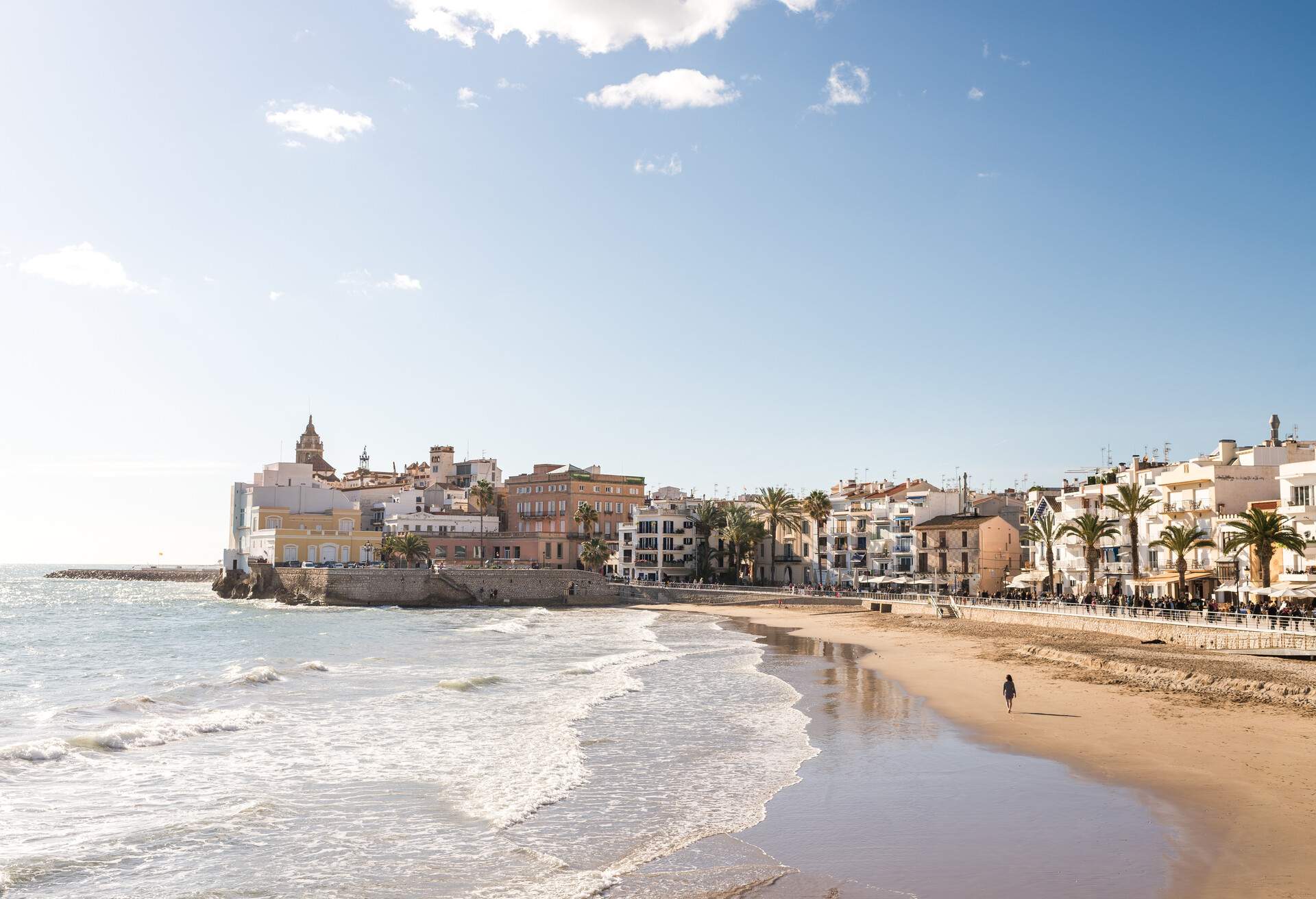 Under the bright sky, a person is strolling along the beach close to the coastal town.