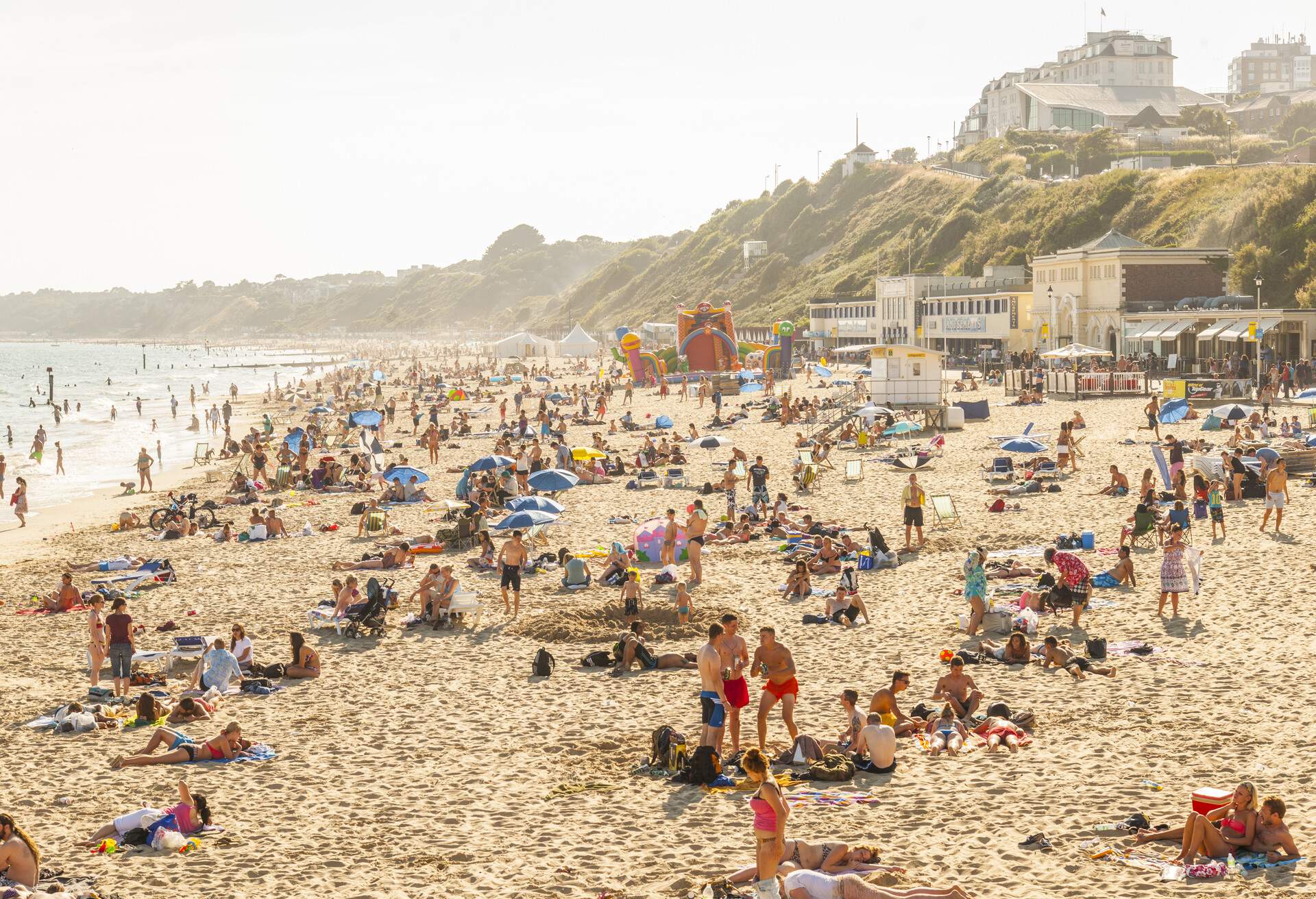 A densely populated sandy beach with structures and buildings atop a vegetated slope.