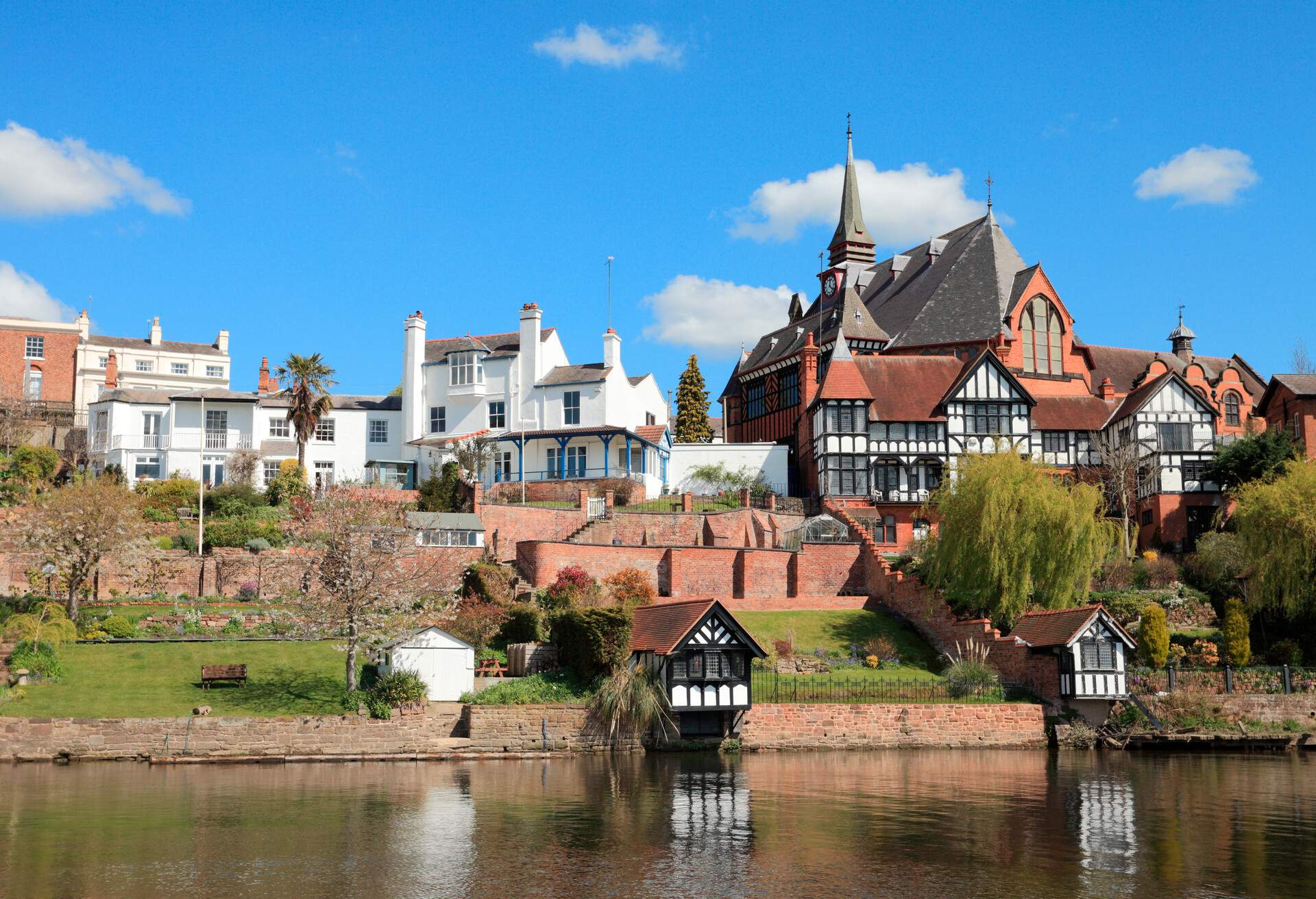 A half-timbered house with a spire next to white buildings in front of a river.