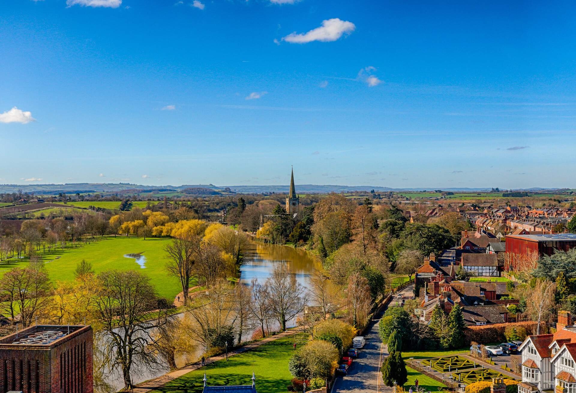 A historic town by the river surrounded by green spaces and trees.