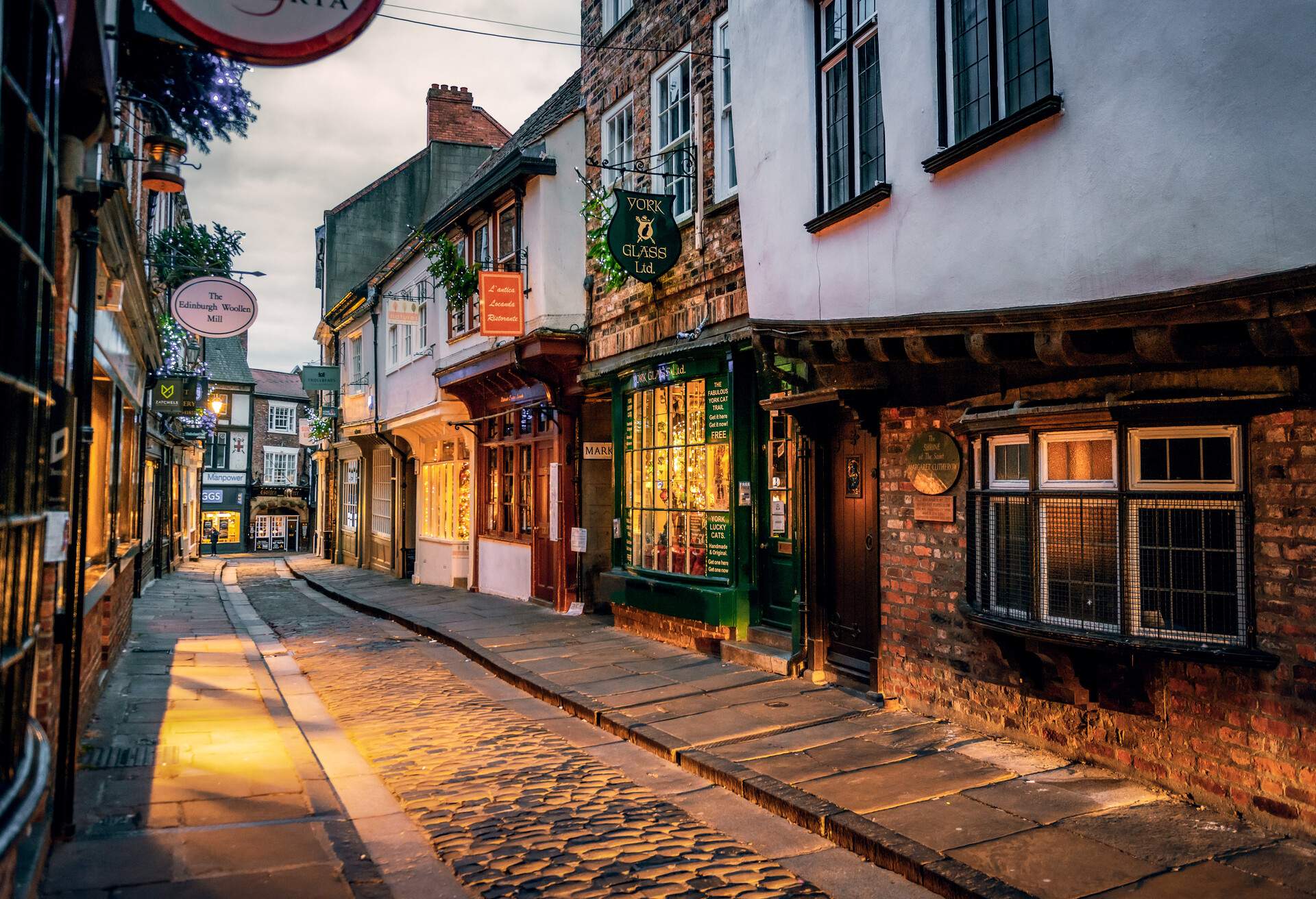 A narrow cobbled alleyway in the middle of medieval buildings houses various shops.