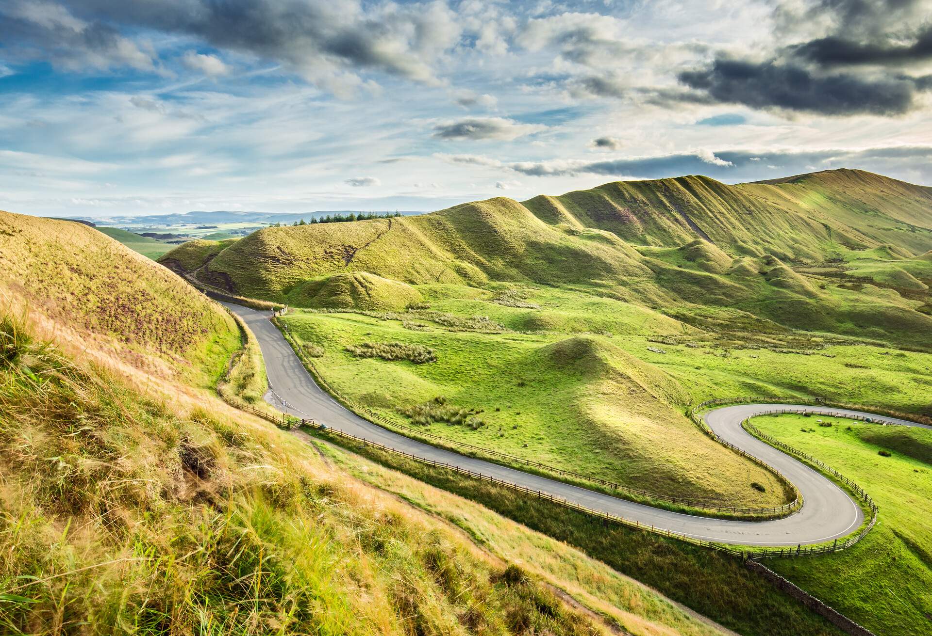 A roadway with a hairpin curve winding through the slopes of grass-covered hills.