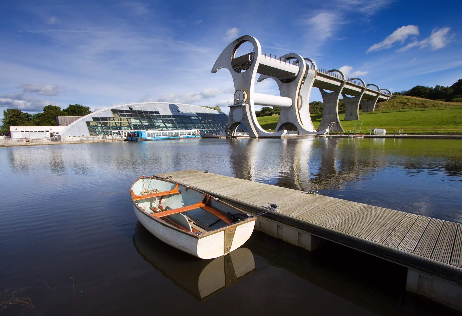 A tiny boat is moored on a boardwalk against the Falkirk Wheel, a spinning boat lift connecting canals on opposing sides of the region. 