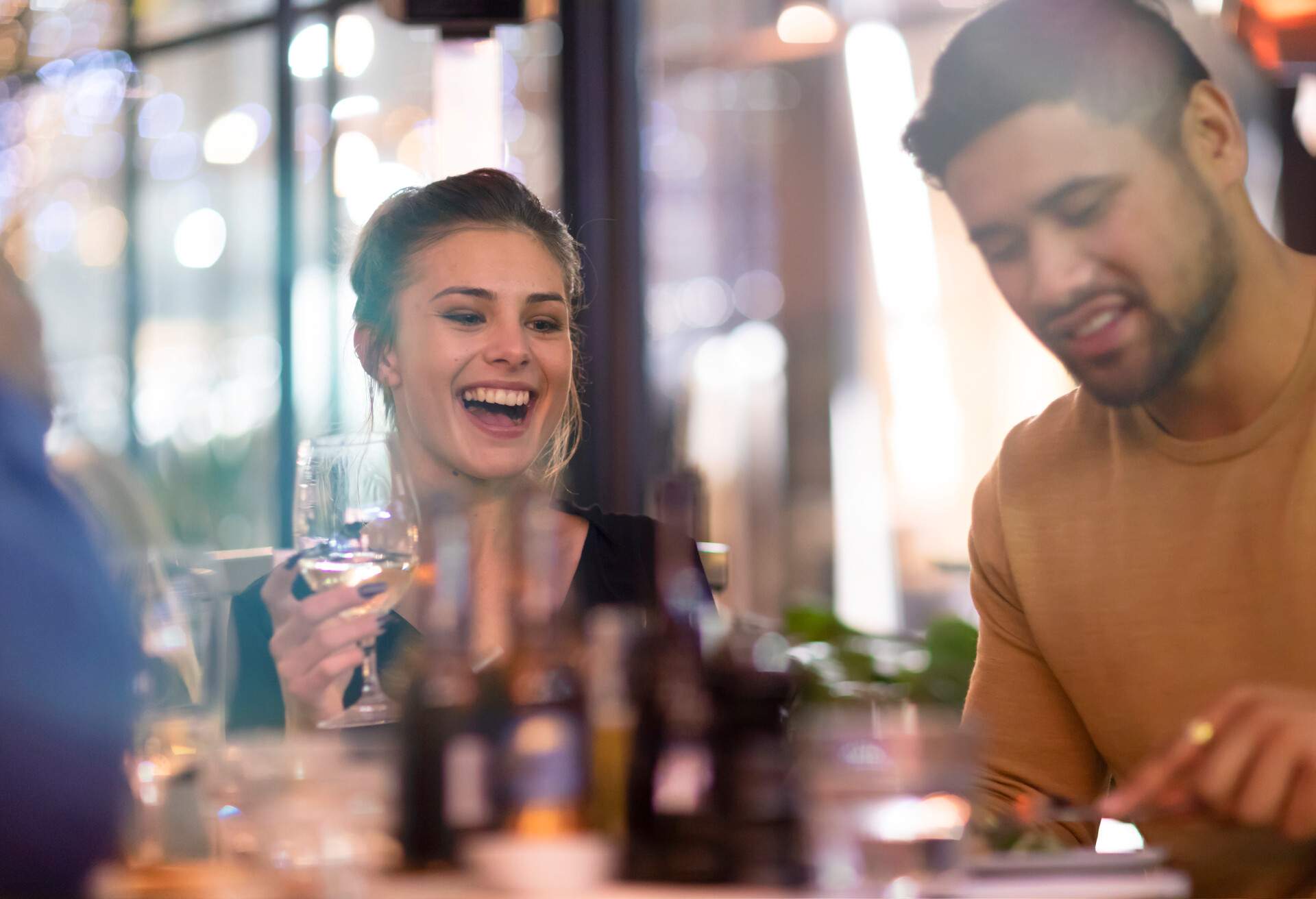 A happy lady holding a glass of wine and his boyfriend having fun dining in a restaurant.