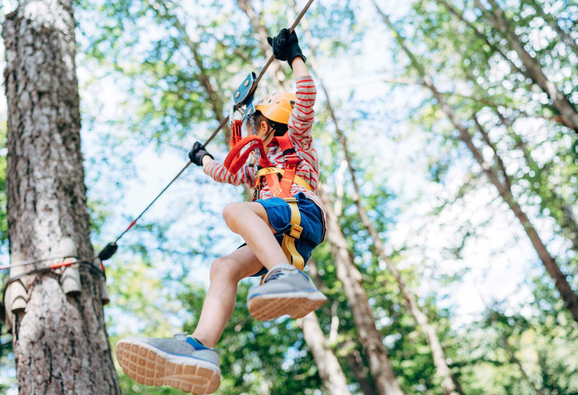 A kid hanging on the zipline holds on to the rope tight approaching a tree.