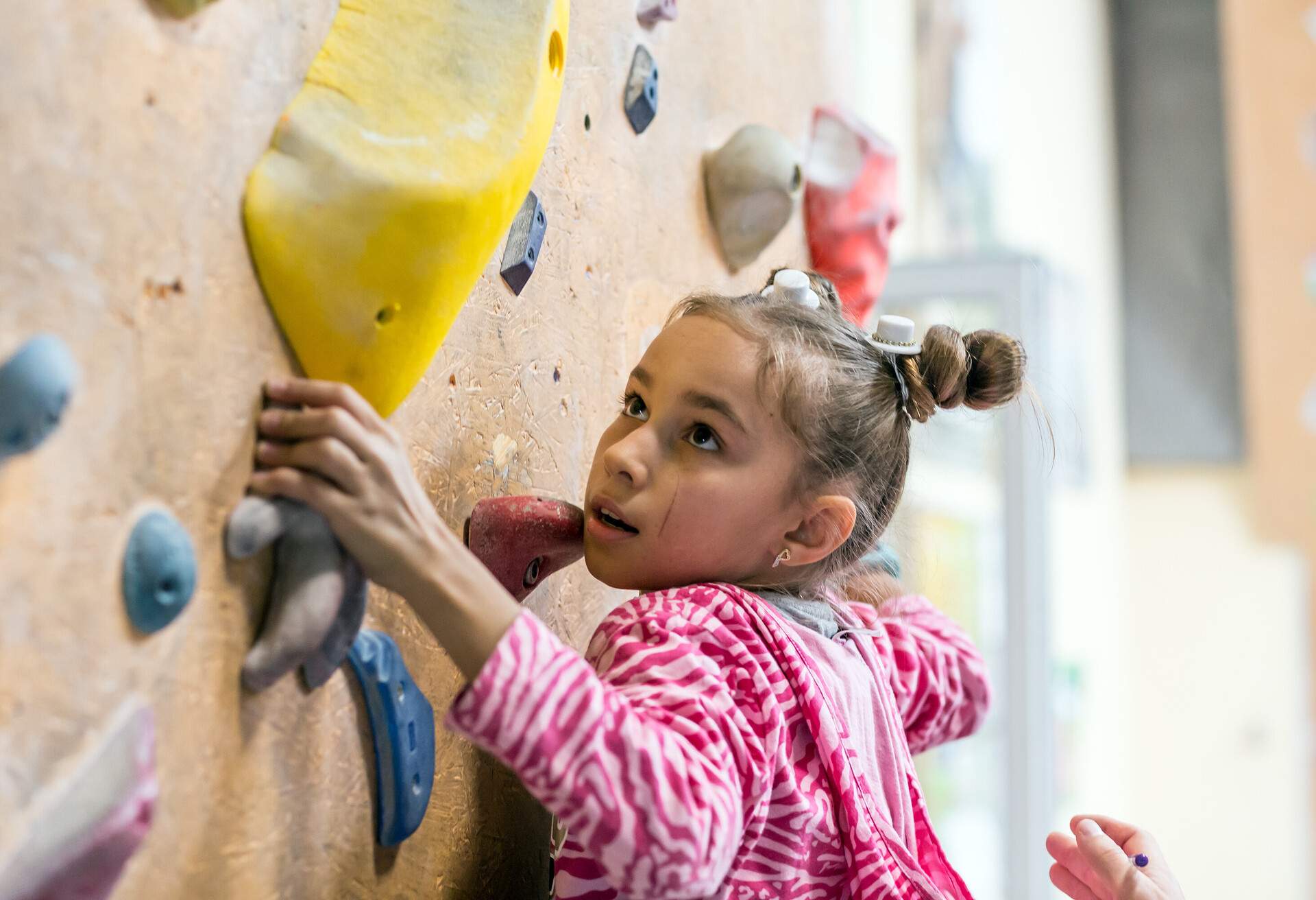 A young girl with a pink and white striped jacket climbing a wall.