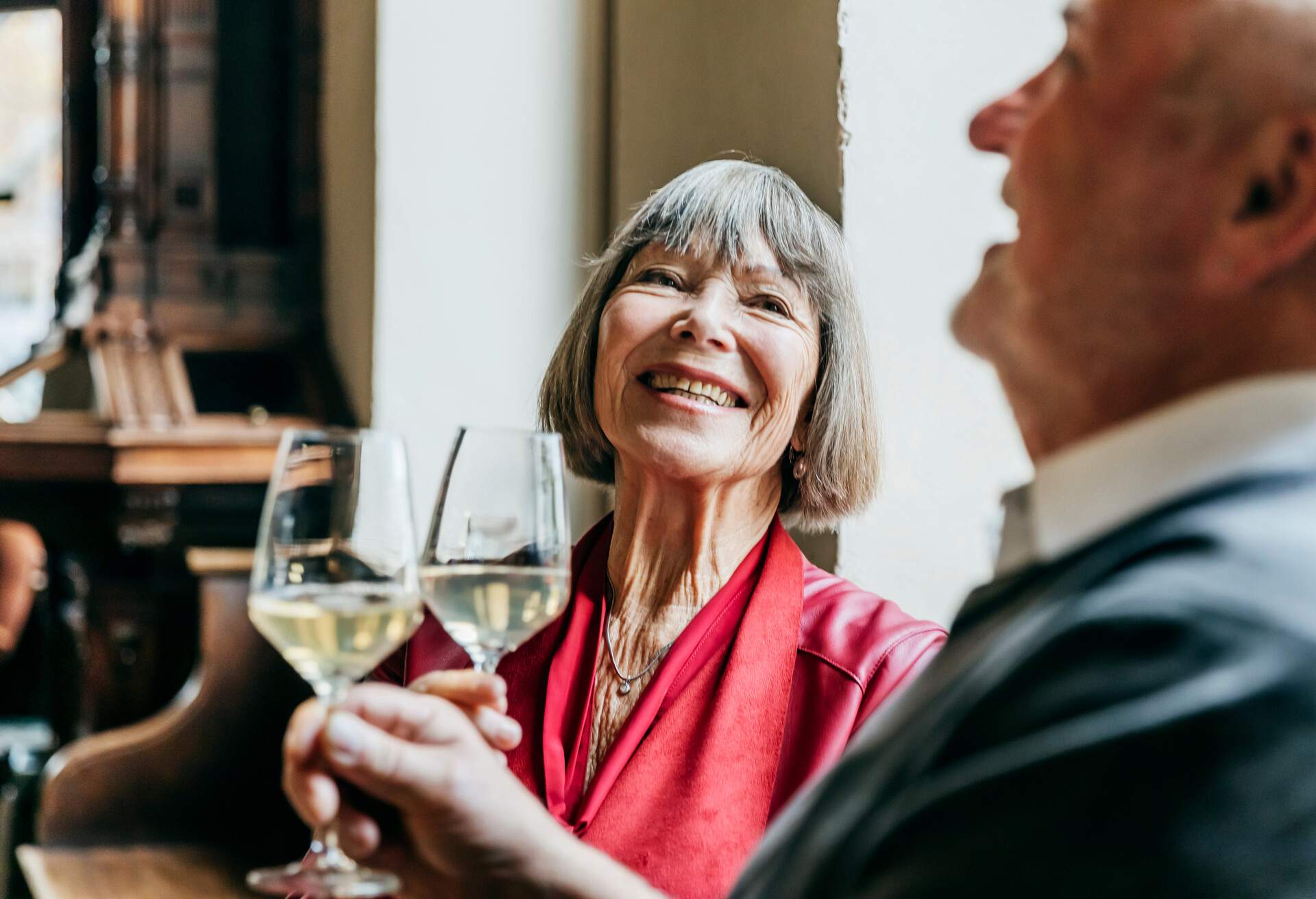 An elderly couple laugh with each other while drinking white wine.