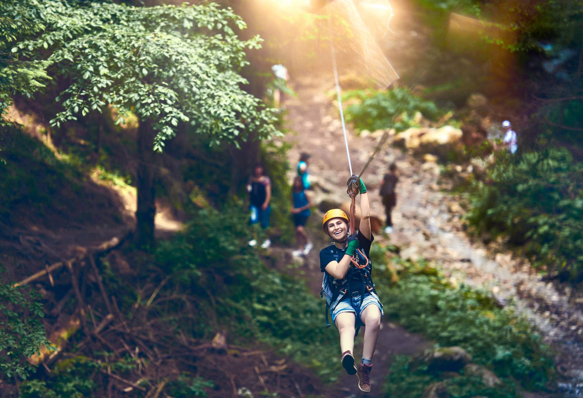 A young woman joyfully traverses a zip line, laughing and enjoying the thrilling adventure, with the natural surroundings beautifully blurred in the background.
