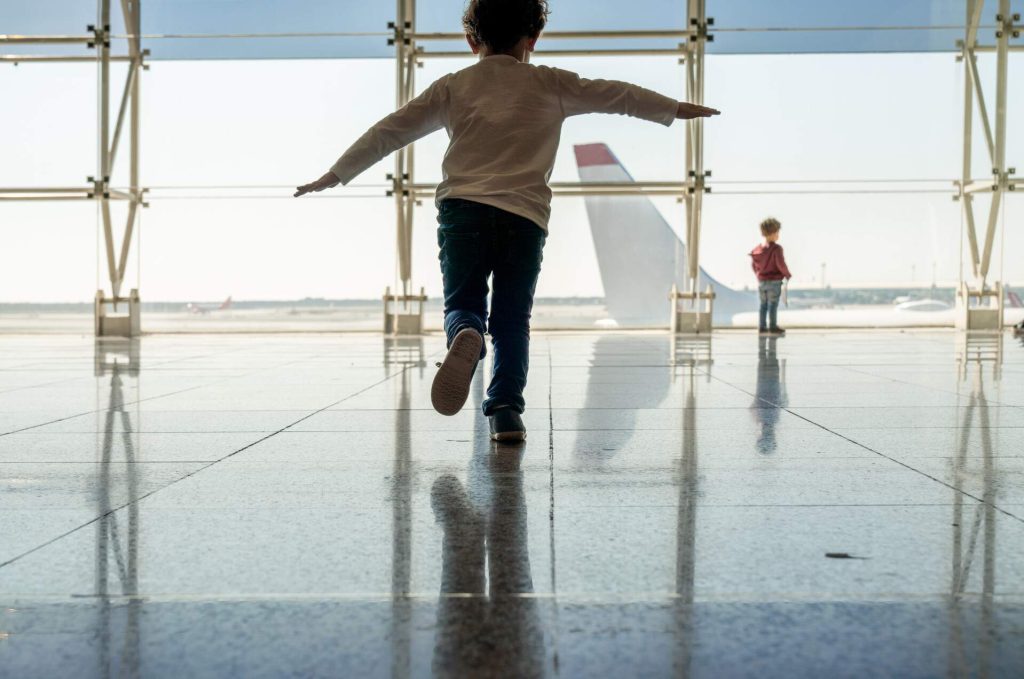 A kid running at the airport with and airplane in the background