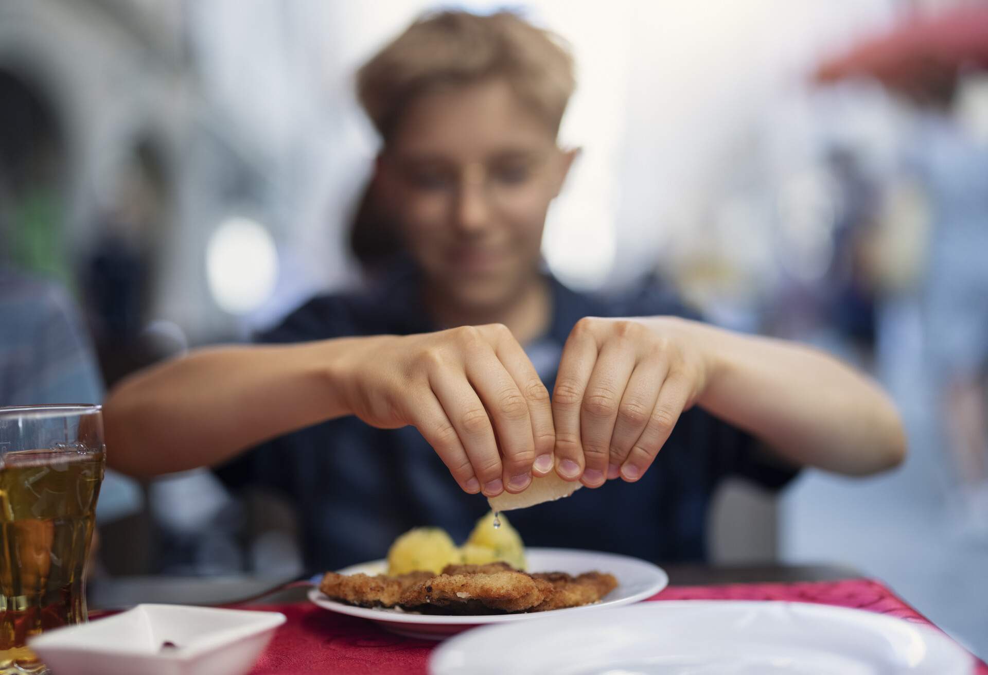 Teenage boy eating wiener schnitzel in a restaurant. The boy is squeezing lemon over the schnitzel.