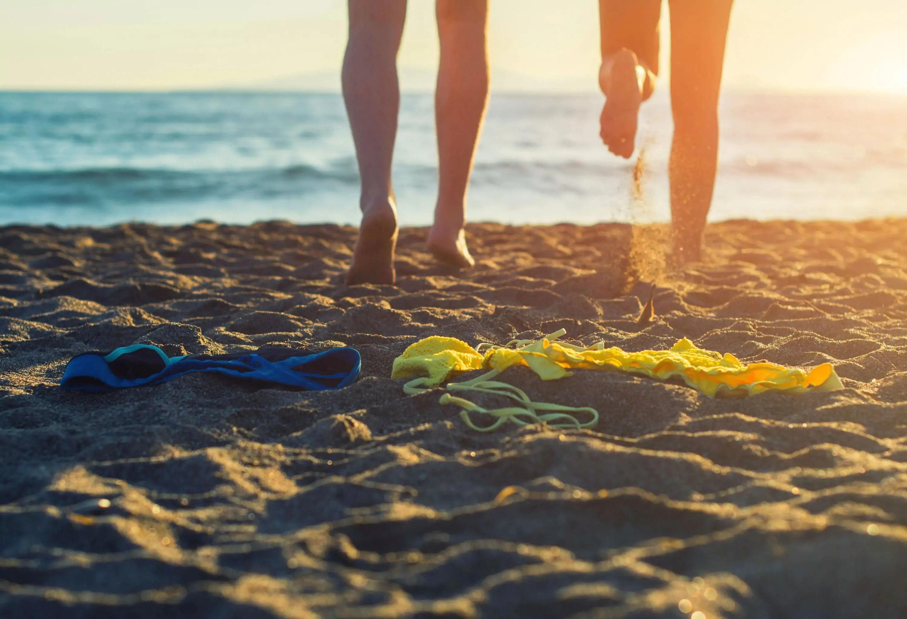 Two individuals run on the beach shore at sunset.