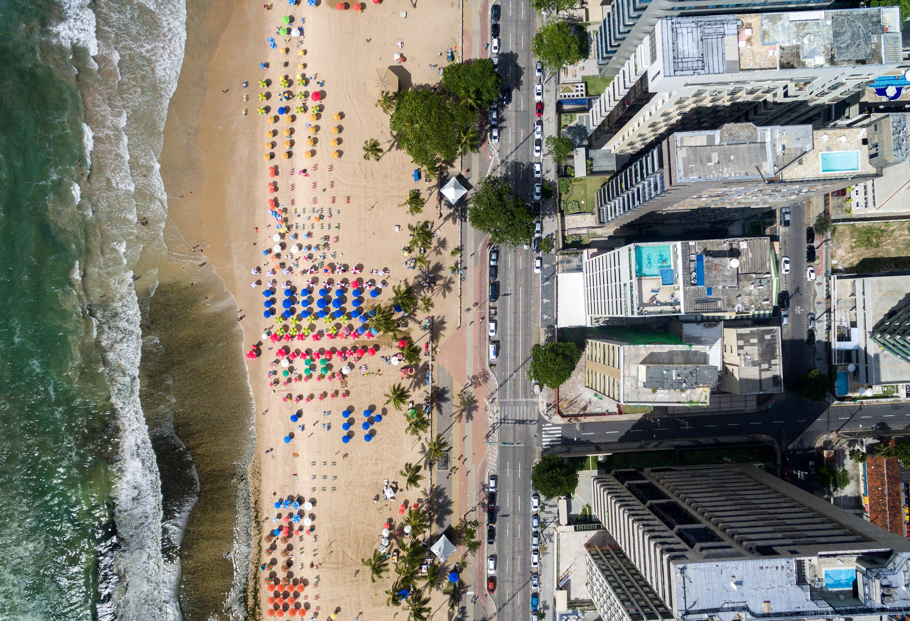 Top view of a beach dotted with colourful parasols and the coastal city with towering modern buildings.