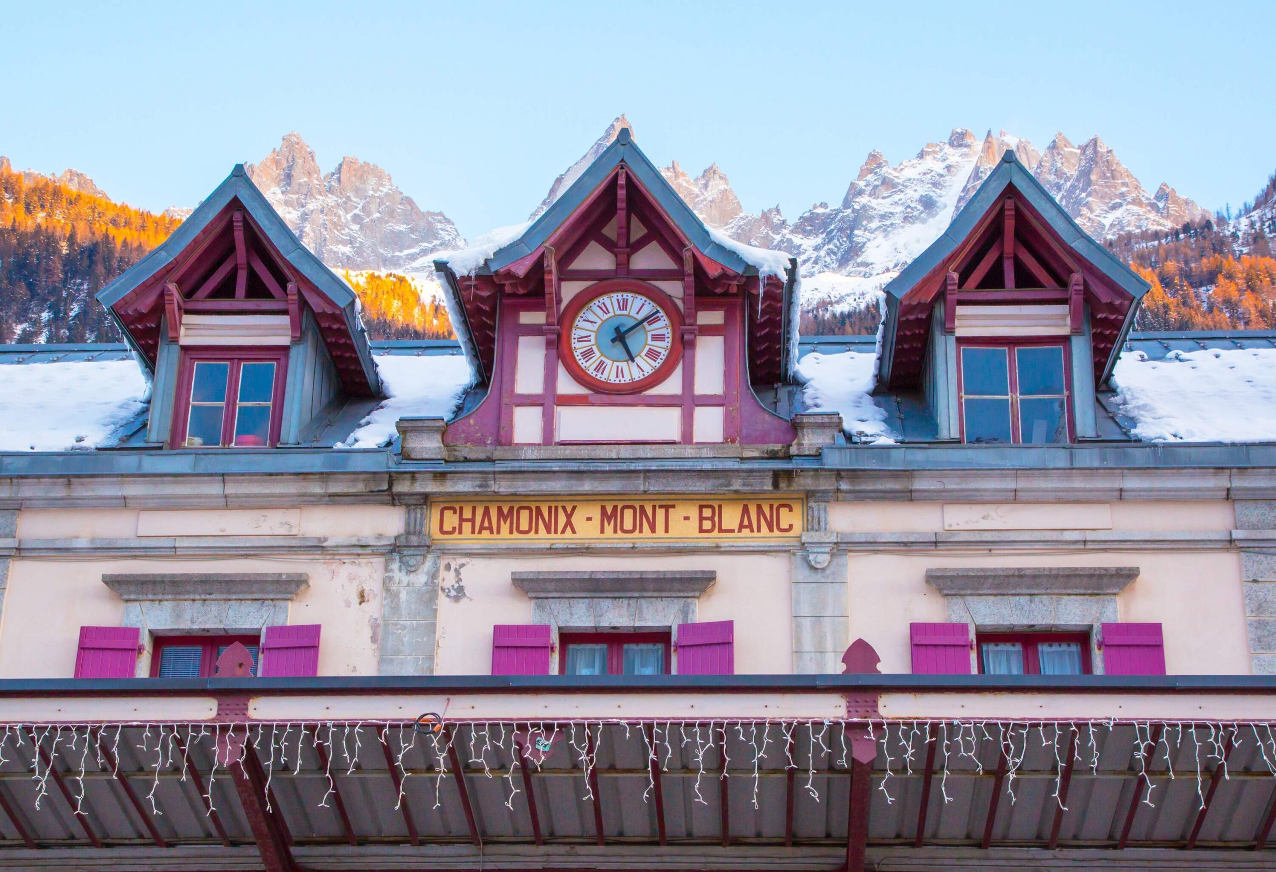 Front of a railway station with the words "Chamonix-Mont-Blanc" in the centre and a snowy mountain in the background. 
