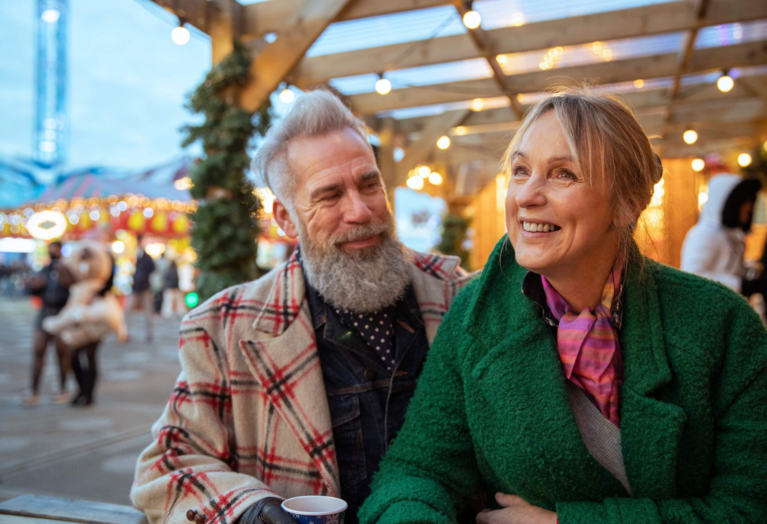 A happy senior couple enjoy drinks at an open air restaurant while at a winter street festival.