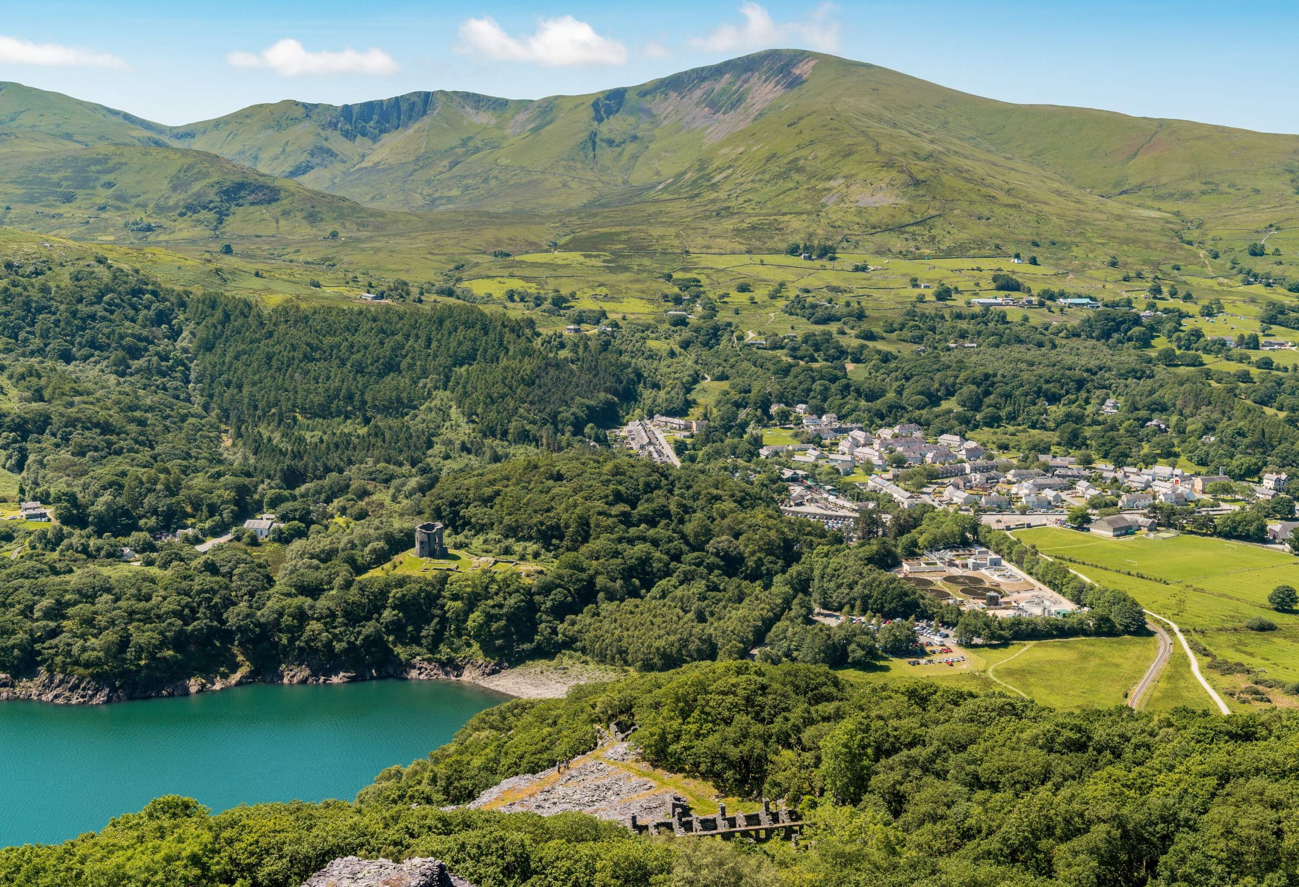 A village in a valley across a lake with banks covered in trees.