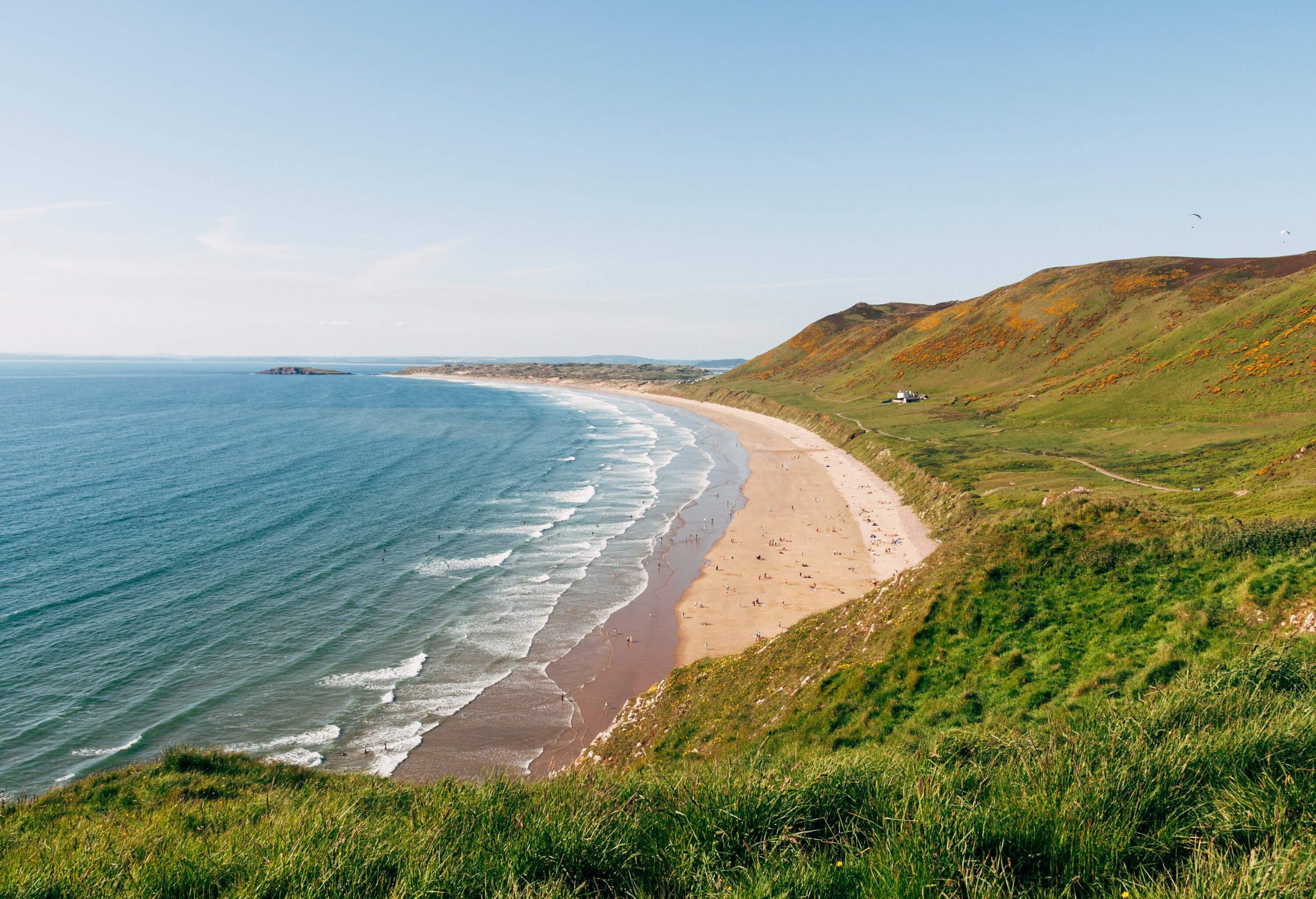 A picturesque long sandy golden shore alongside cliffs at the foot of lush mountains.