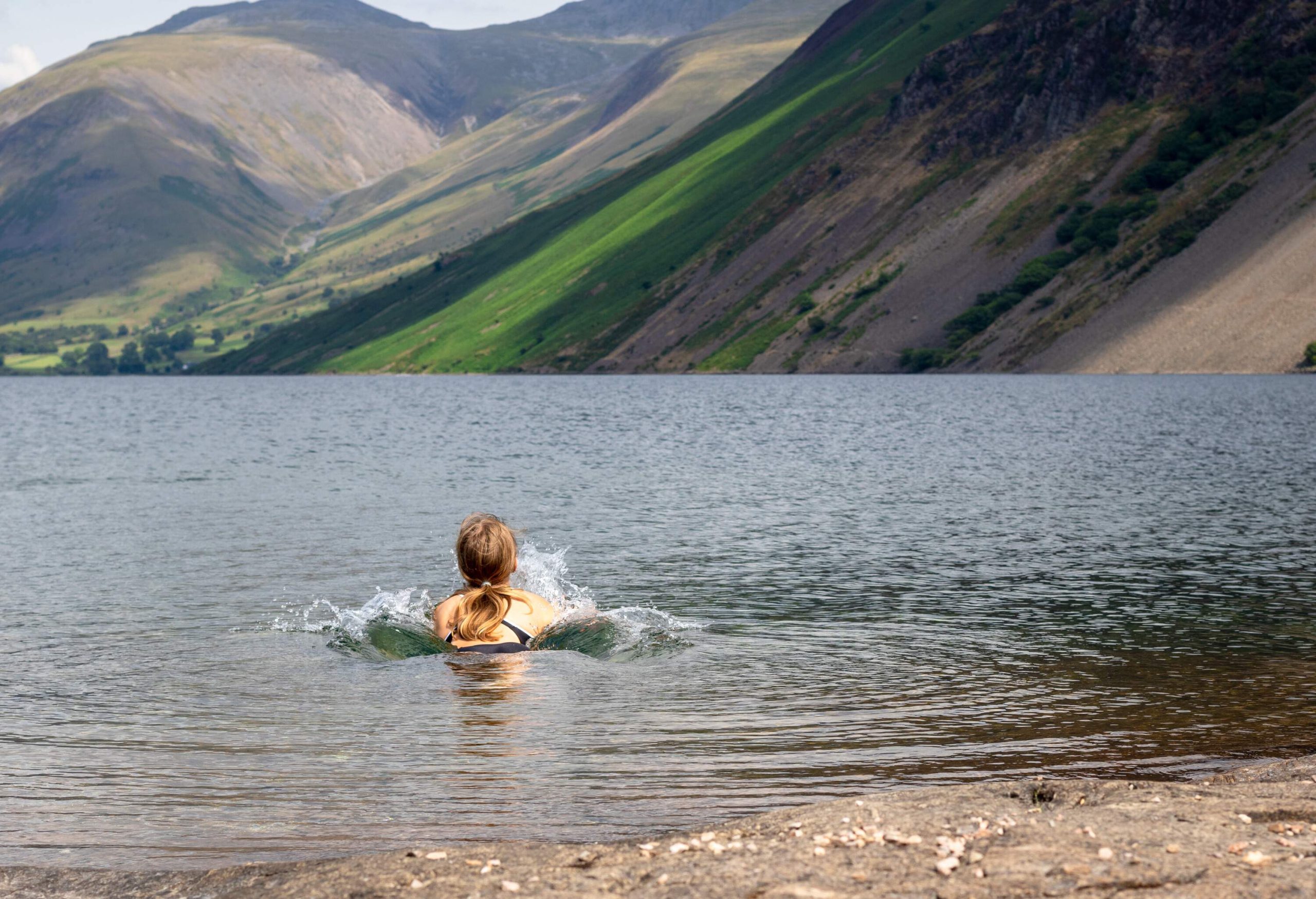 Beautiful landscape view of Wast Water in the Lake District National Park in the UK. A girl relaxing and enjoying refreshing bath in cold water on a beautiful sunny day.