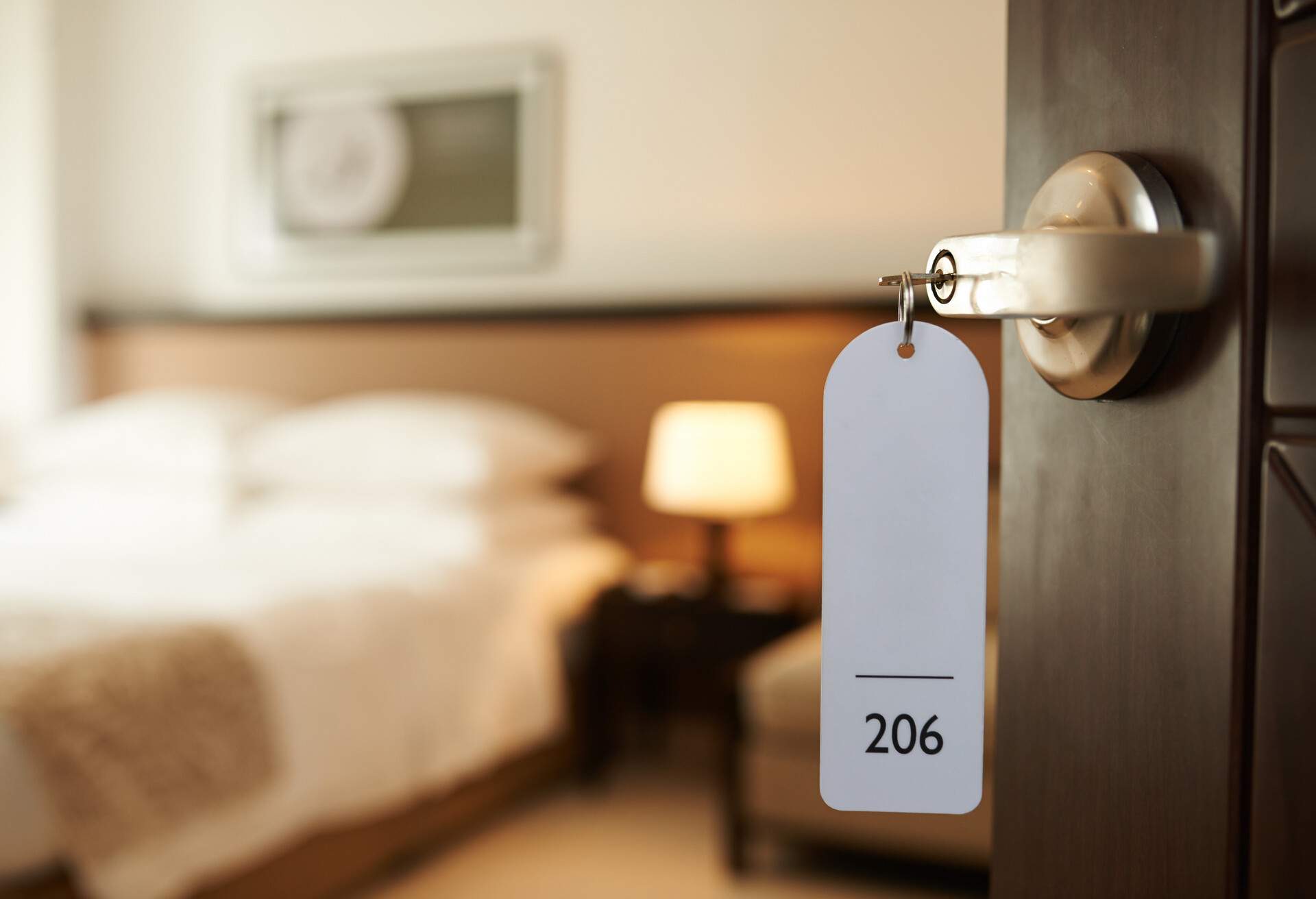 An unlocked hotel room door with the key bearing the number "206" remaining in the lock.