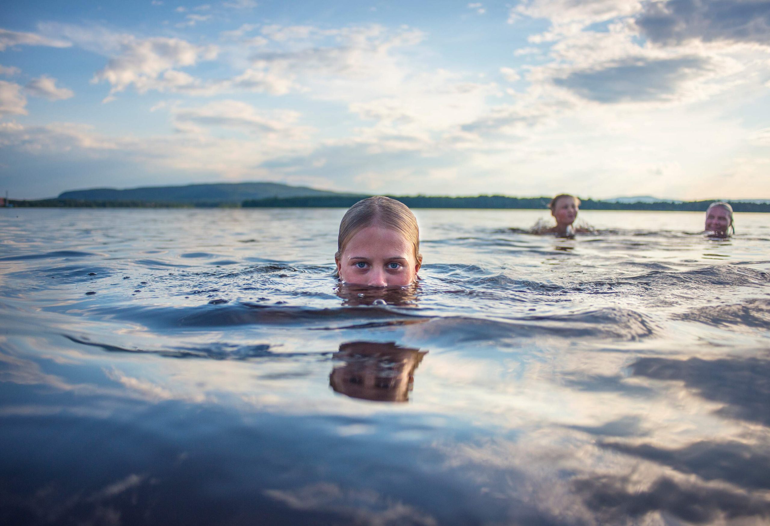 Three people swimming in a lake with their heads poking out of the water.