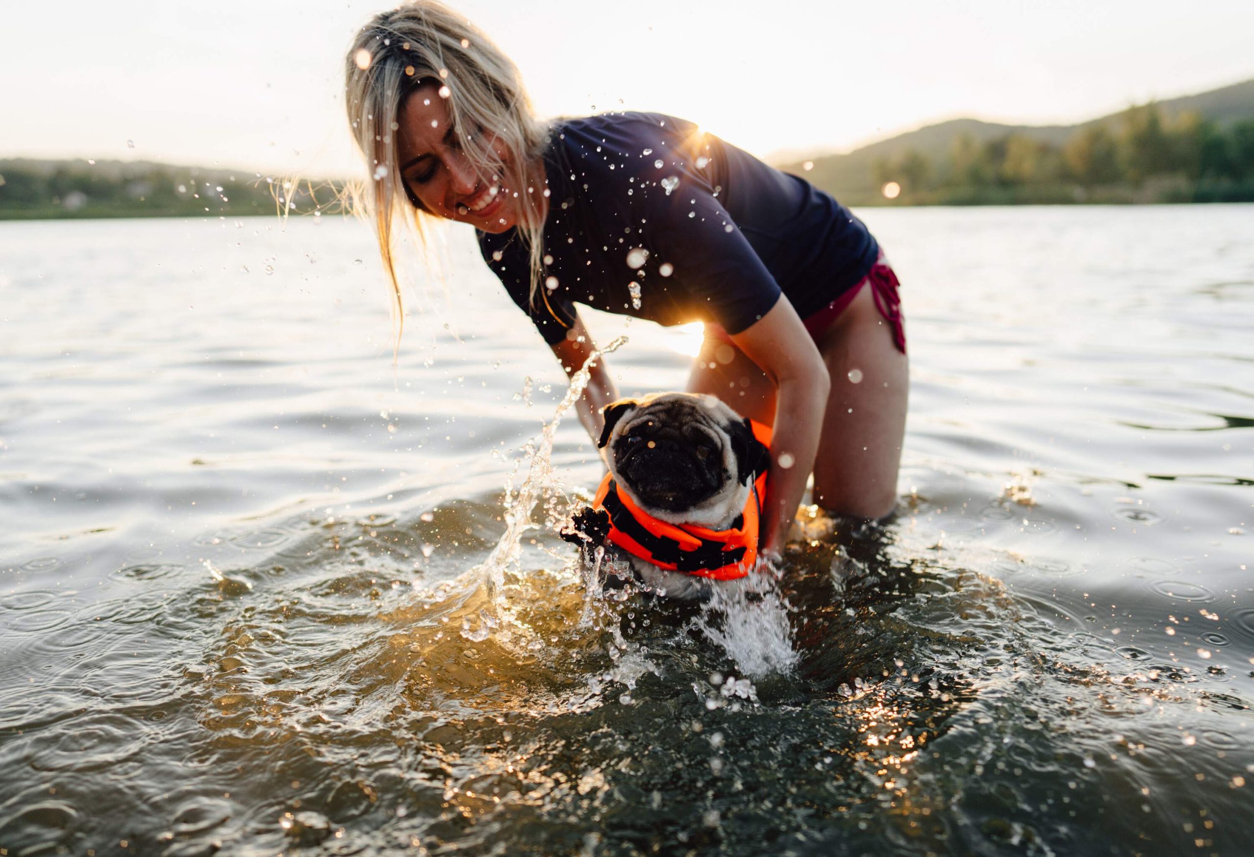 A woman helping her dog in a life jacket swim in the water.