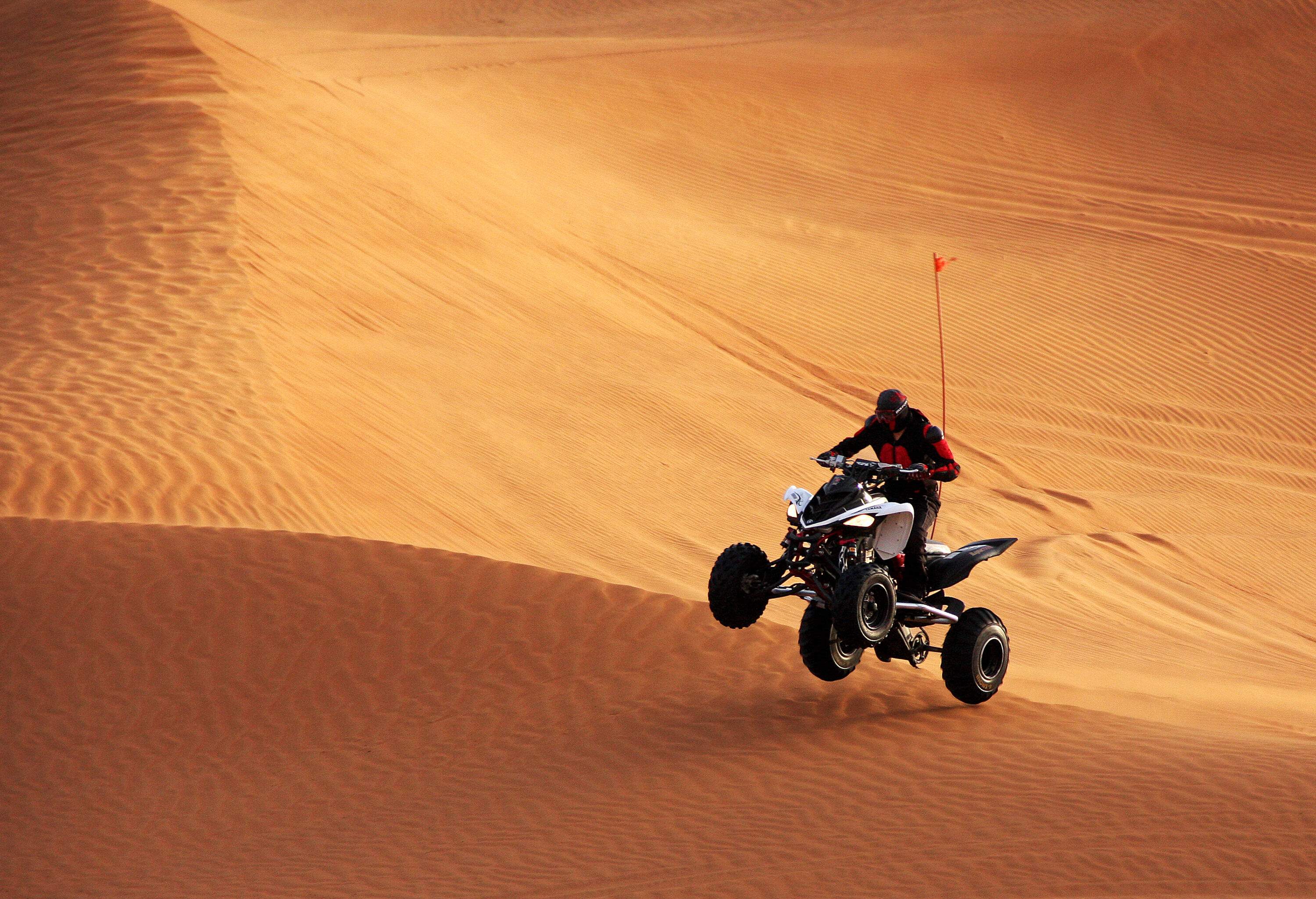 A man in black safety gear performs feats on a quad bike in the desert.