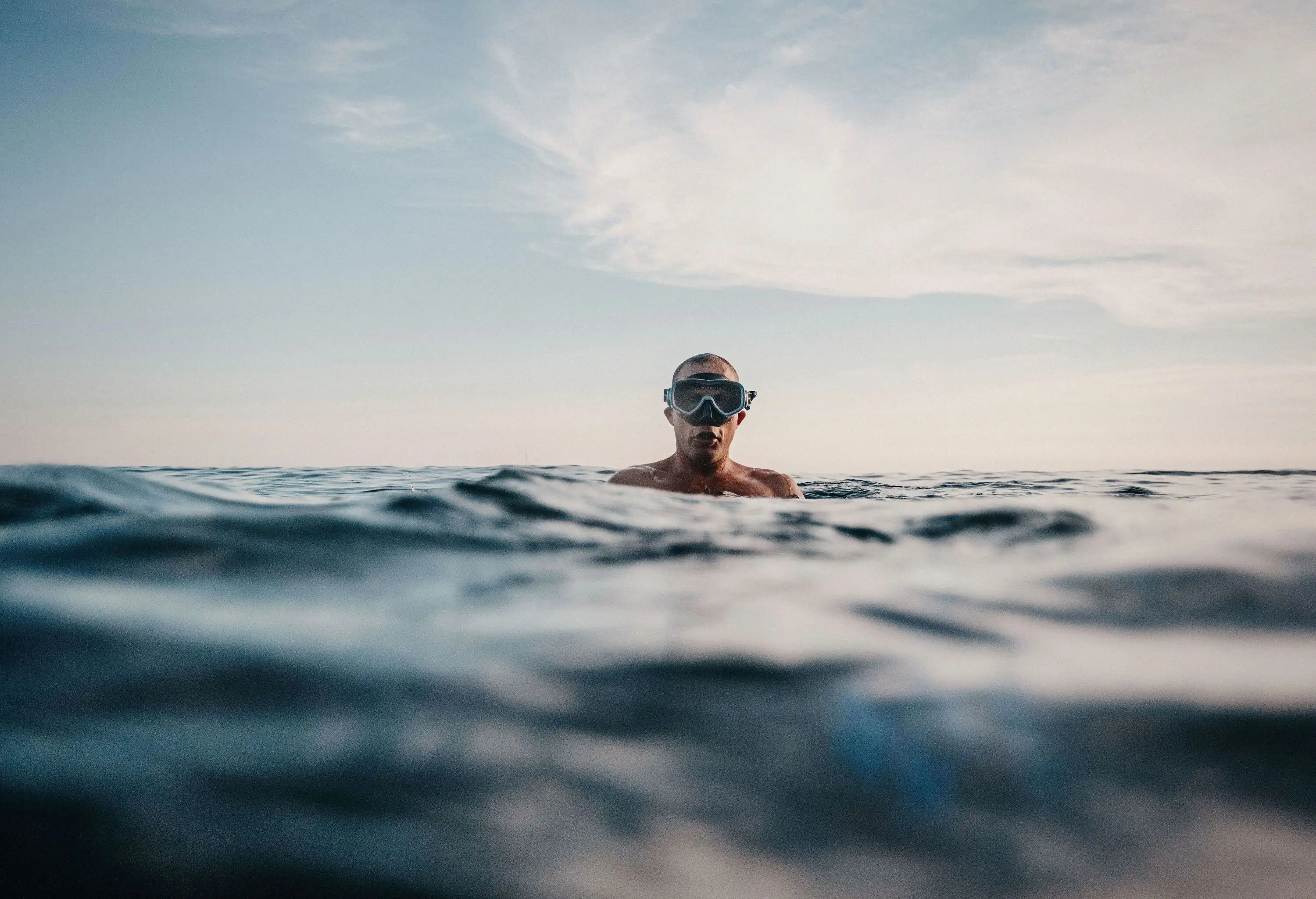 A man wearing a scuba diving mask is half submerged in the water.