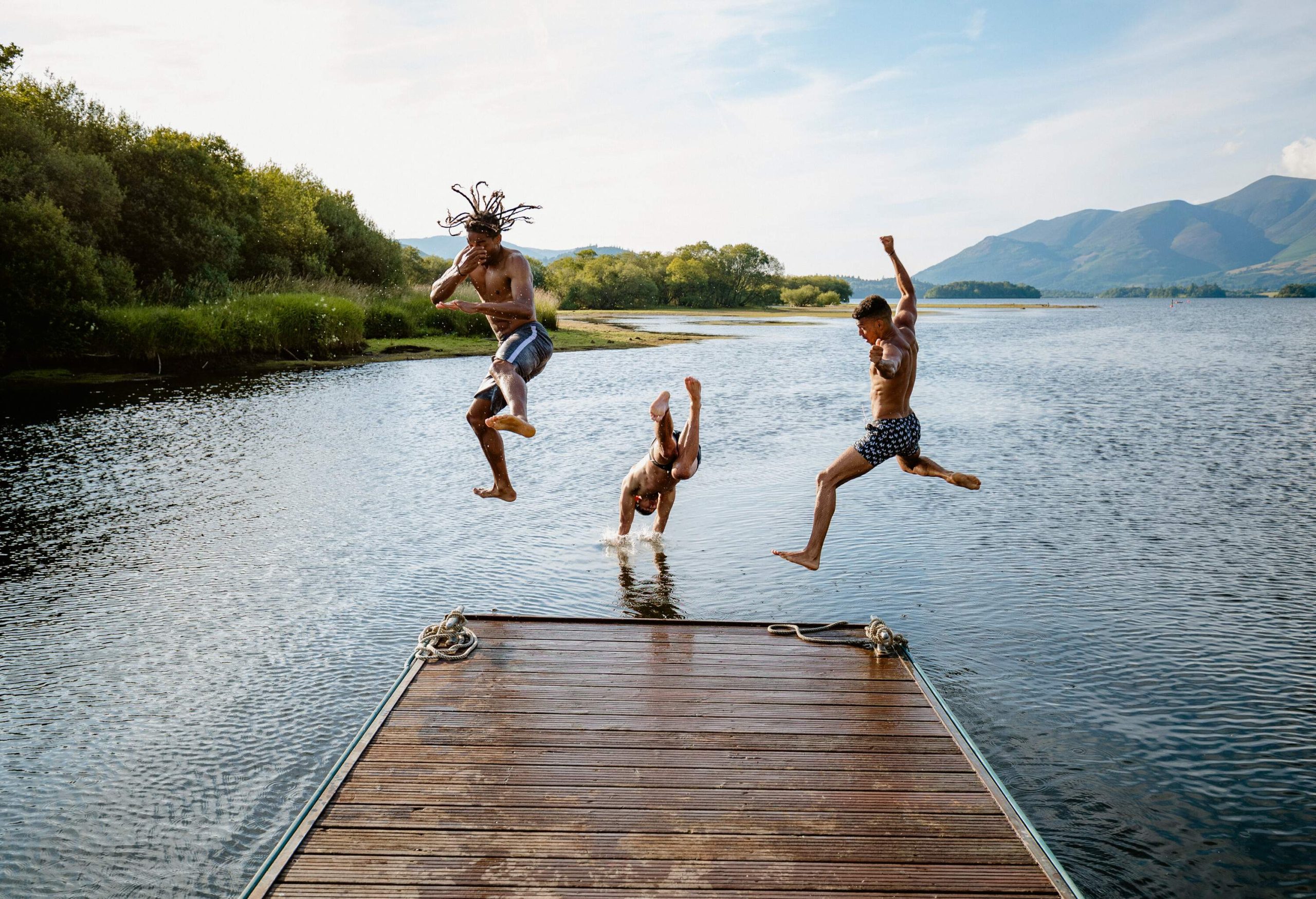 Three people jump into a lake from a jetty.