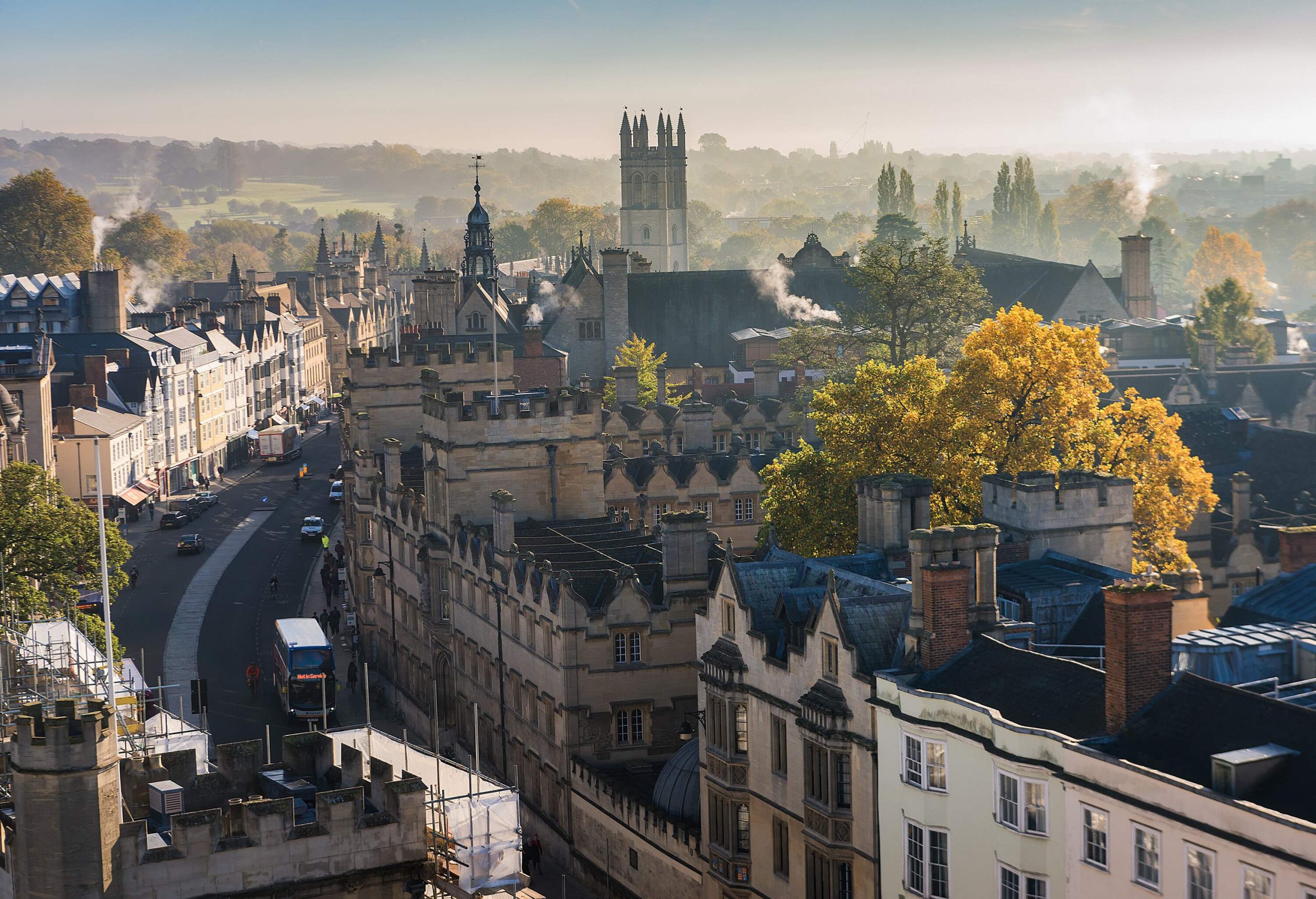 Aerial view of an old town with classic buildings surrounded by tall trees on a hazy day.