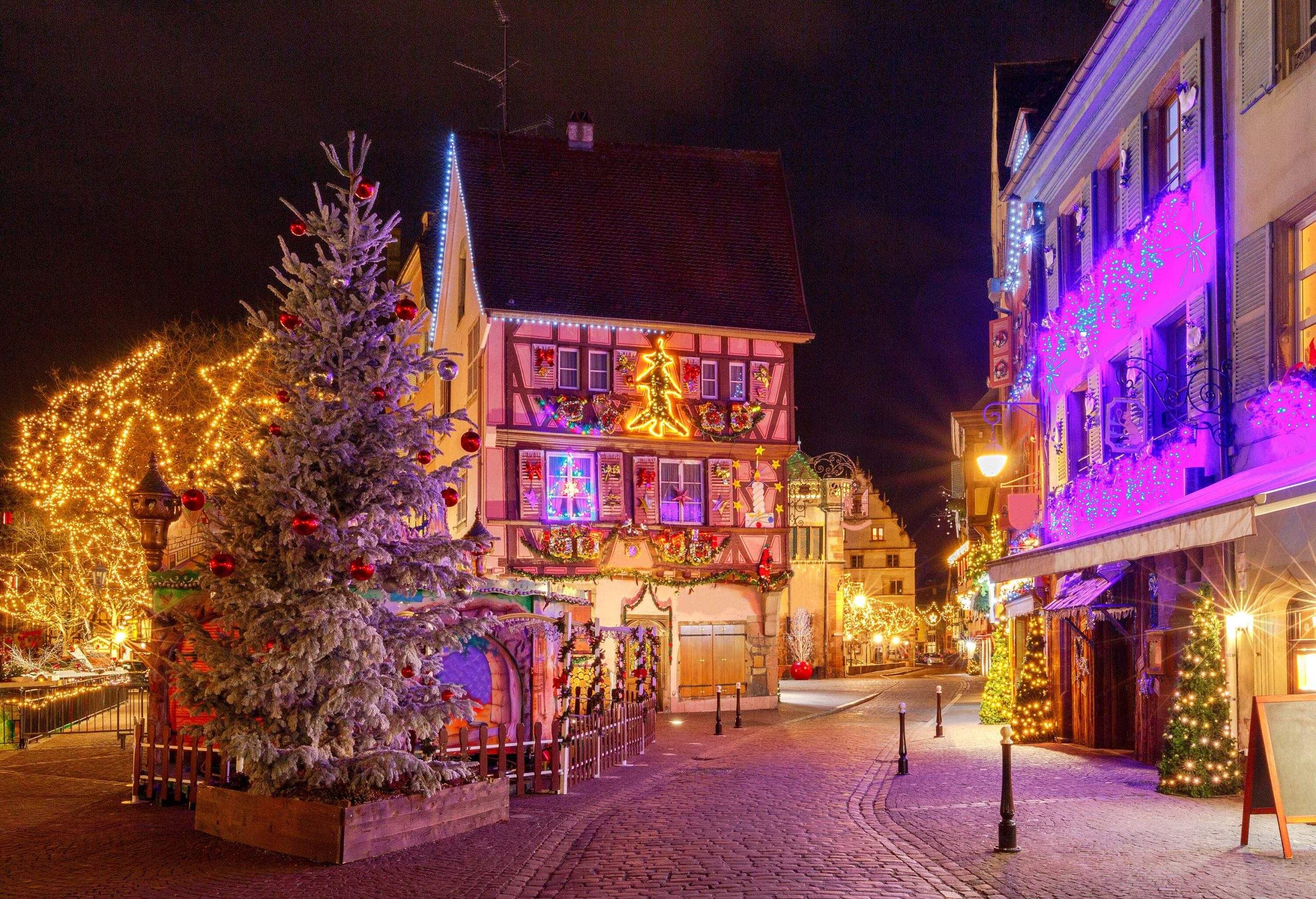 A street of traditional old half-timbered houses decorated with colourful Christmas lights and various Christmas ornaments.