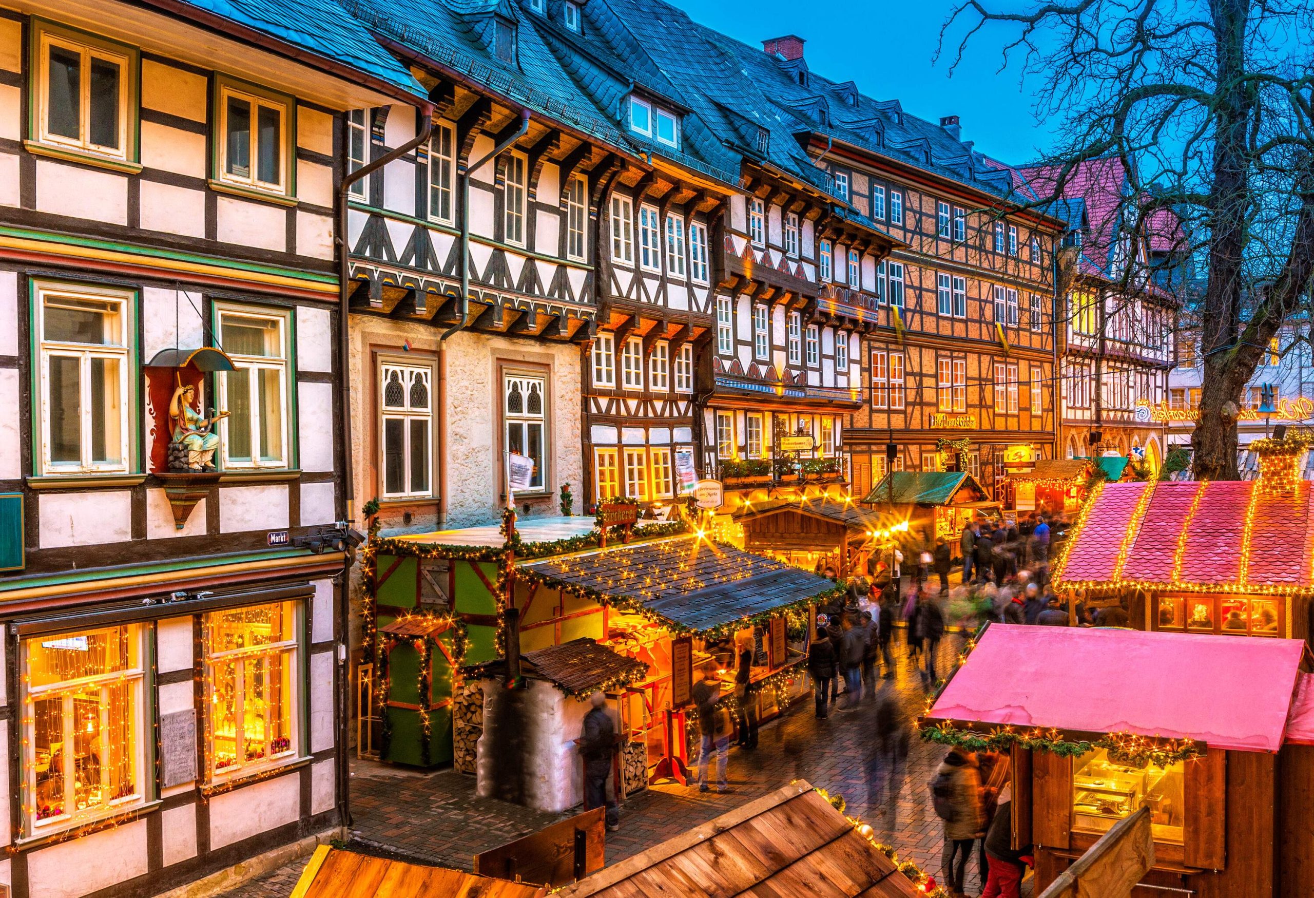 Half-timbered buildings behind Christmas shops decorated with lights.
