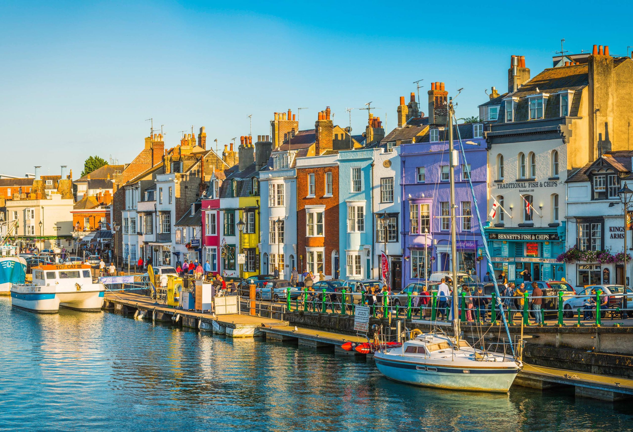 A lively coastal town with boats lining the harbour and brightly coloured buildings along the shore.