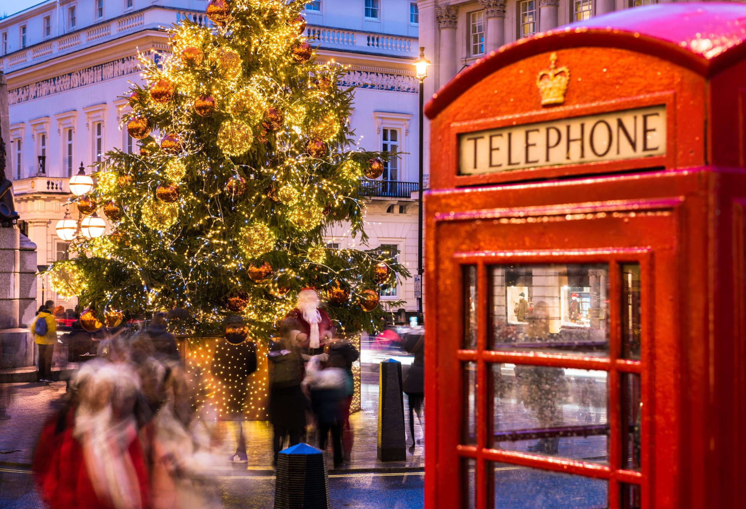 People in motion under giant illuminated Christmas lights and an iconic London telephone booth.