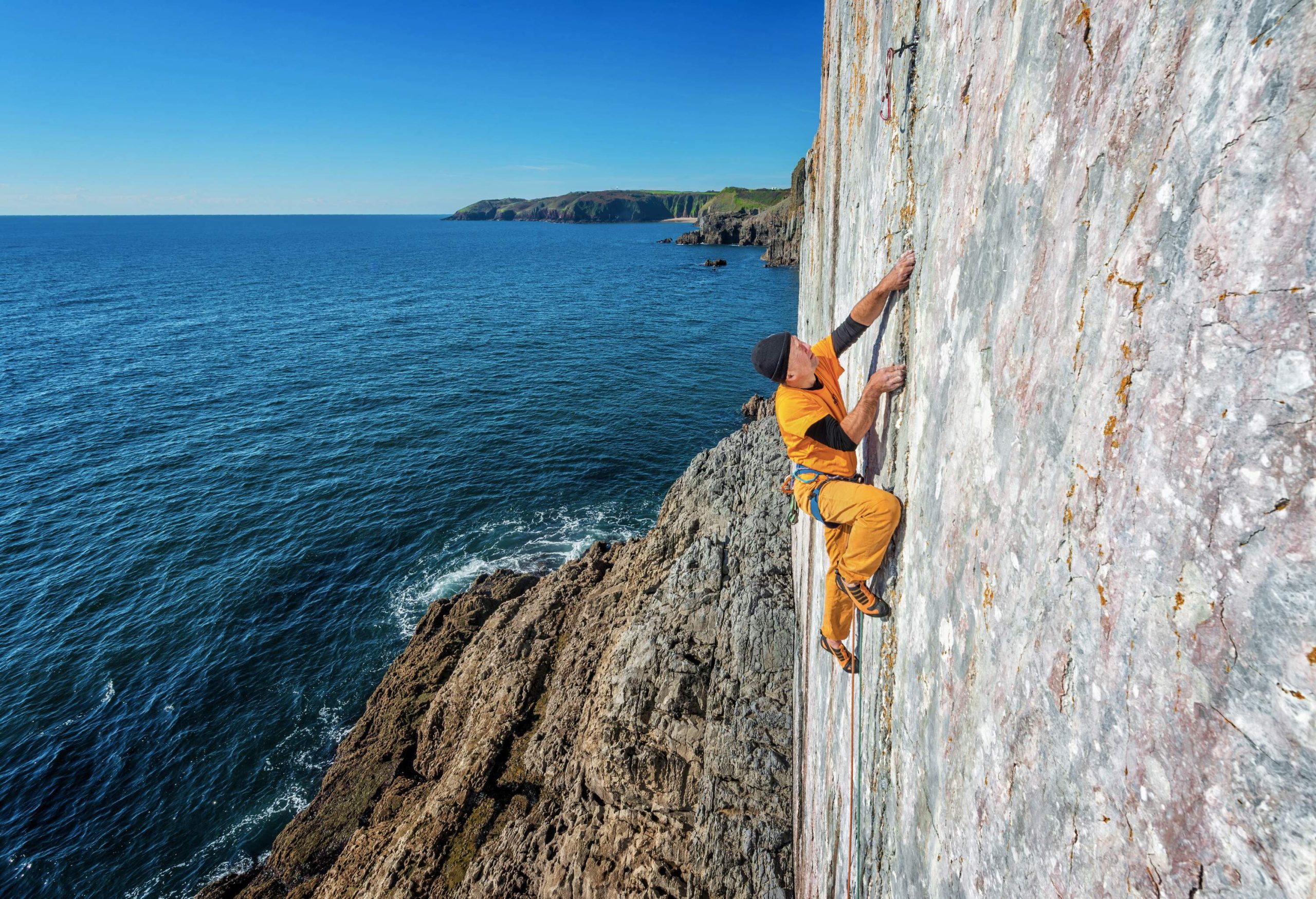 A man climbs the rock cliff alongside the sea.