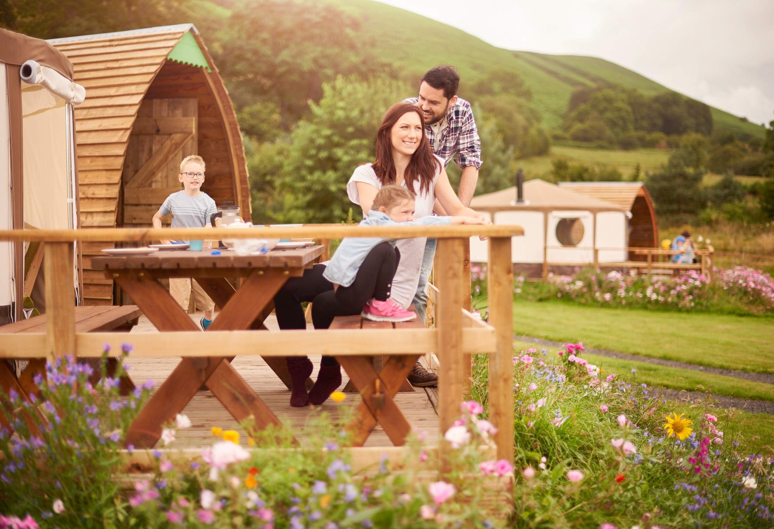 A happy family of four sitting on the terrace outside their yurt tent surrounded with lush and colourful blossoms.