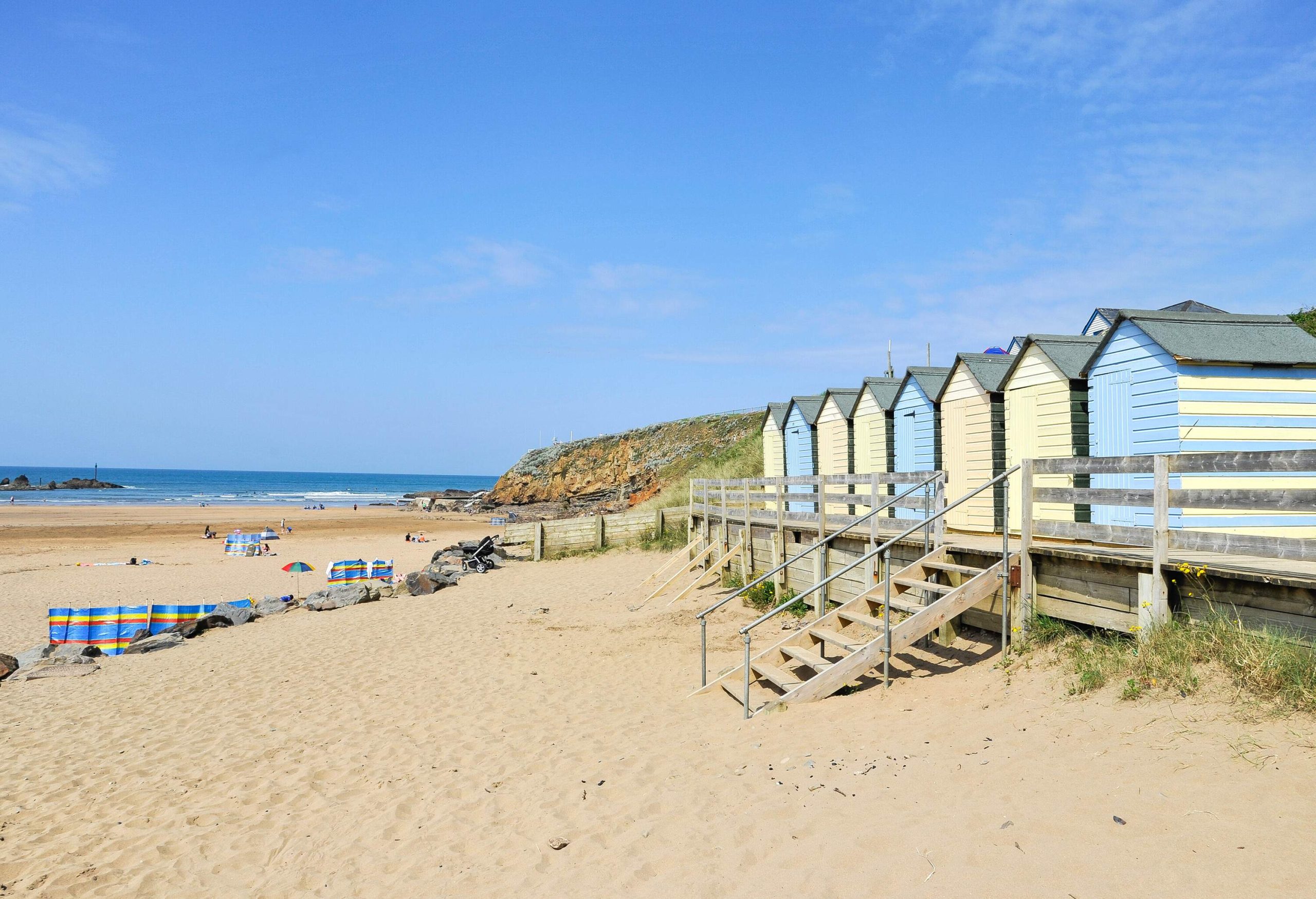 A sandy shore with colourful beach huts against the clear blue sky.