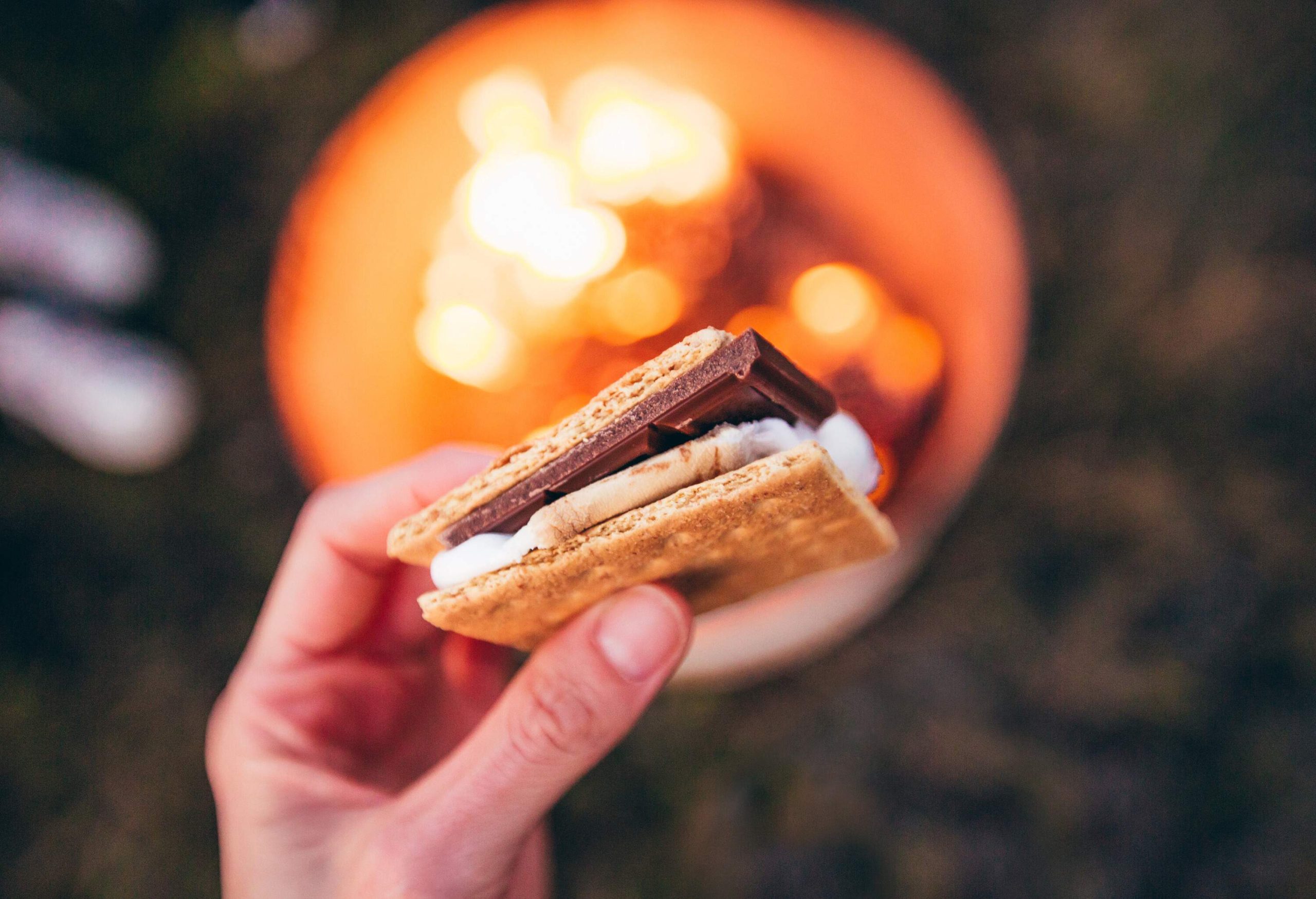 A hand holding a gooey s'more with toasted marshmallow and melting chocolate.