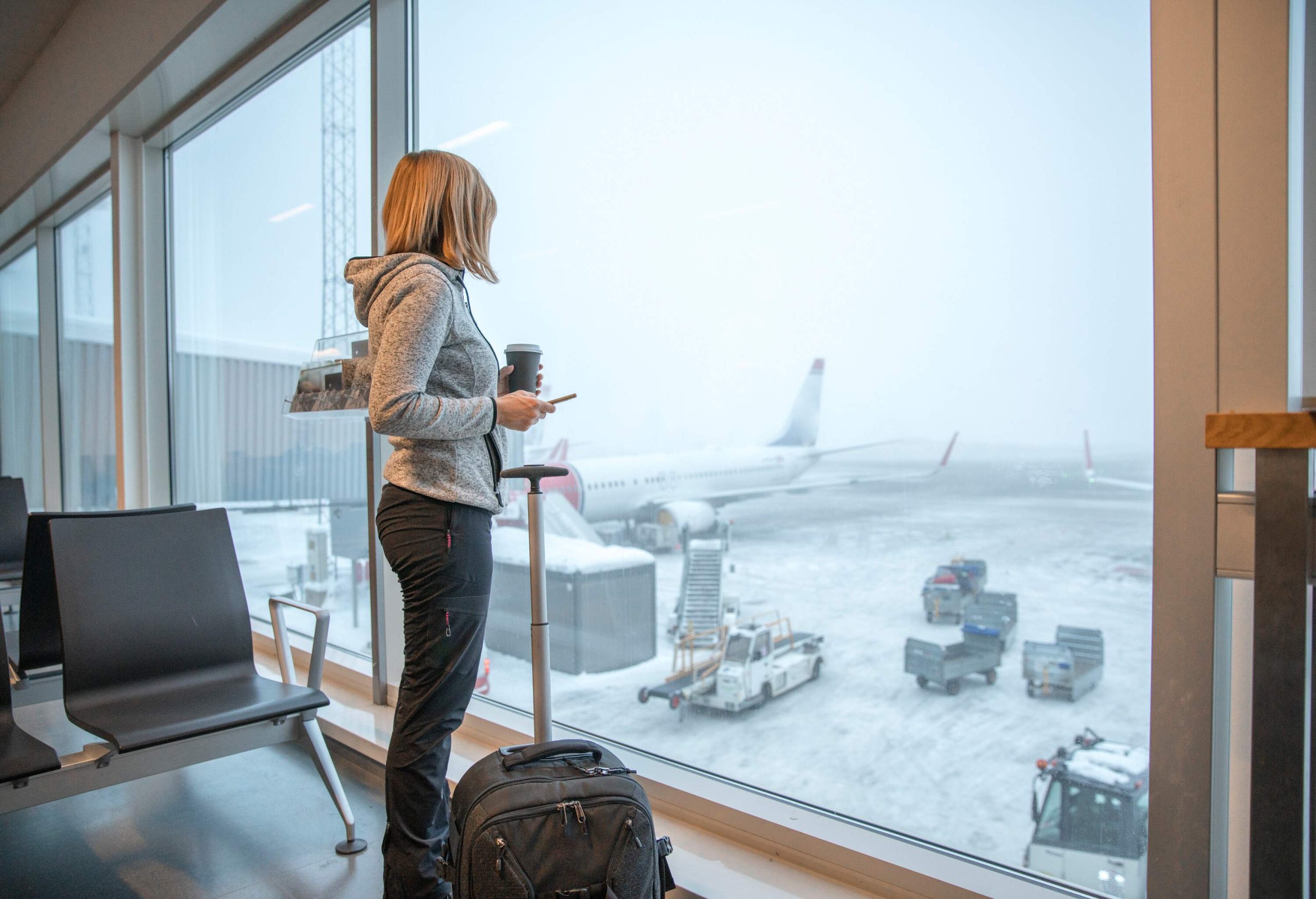 Woman standing close to window with luggage at airport.
