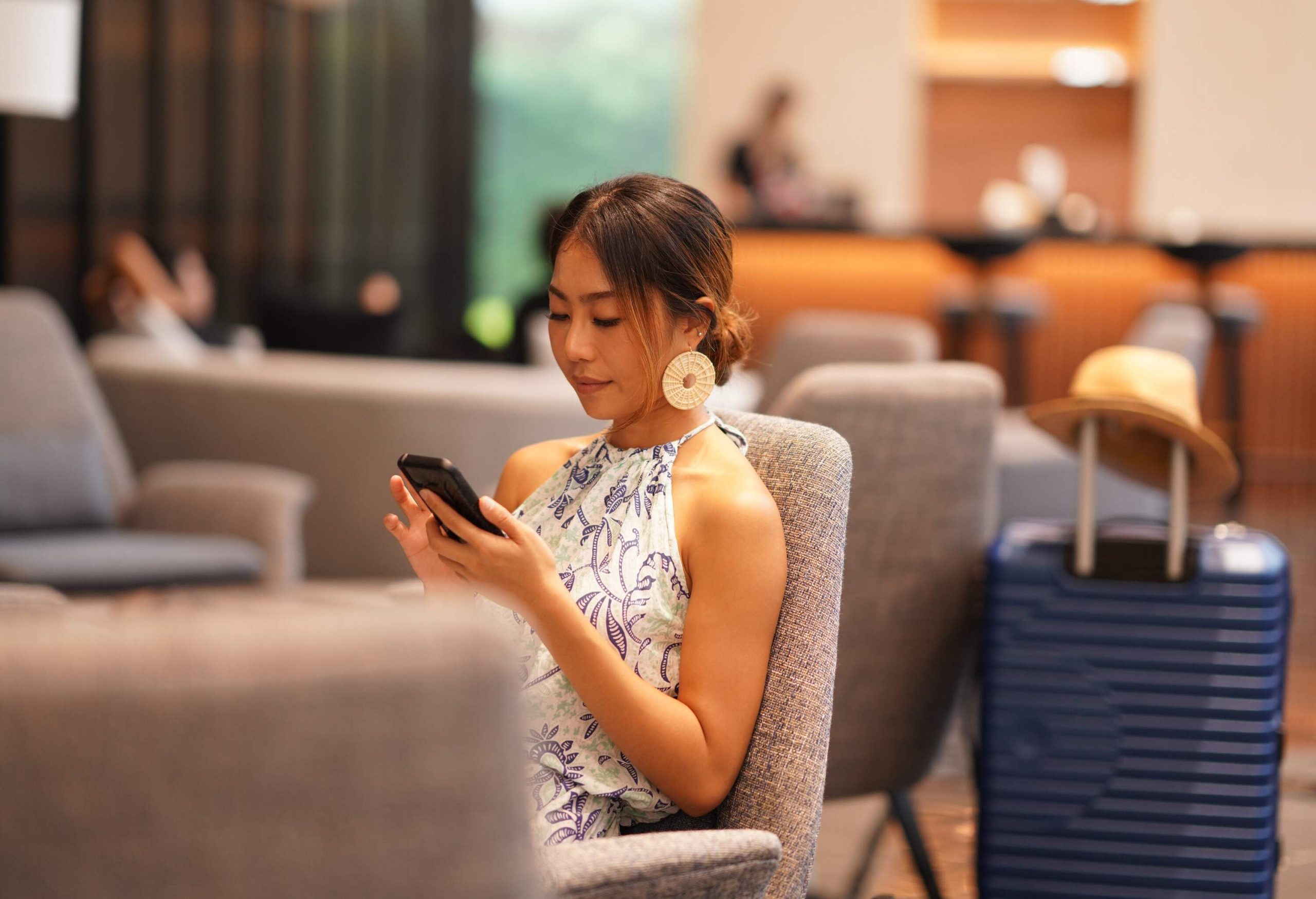 Asian young woman sitting at airport terminal lounge and using phone to chatting.