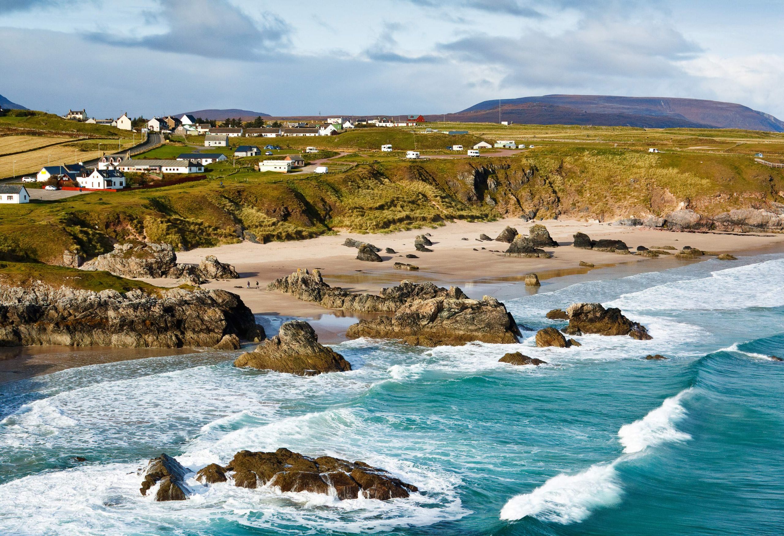 A village with a rocky coastline pounded by crashing waves.