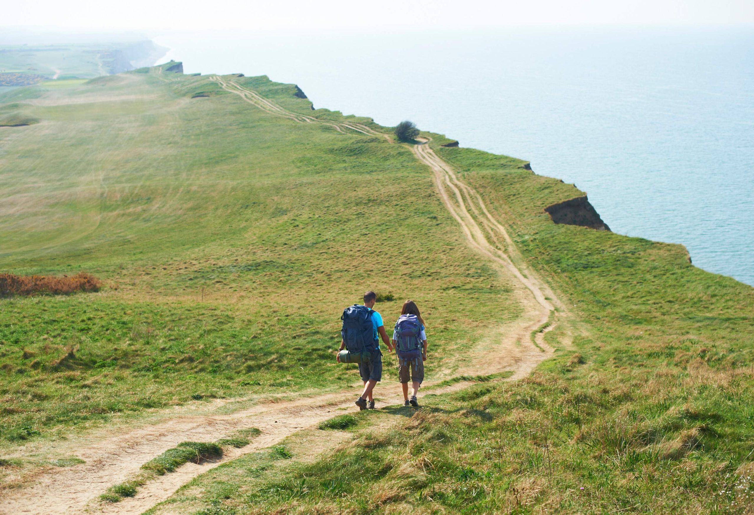 A couple hiking on a path beside a steep cliff with views of a vast ocean.