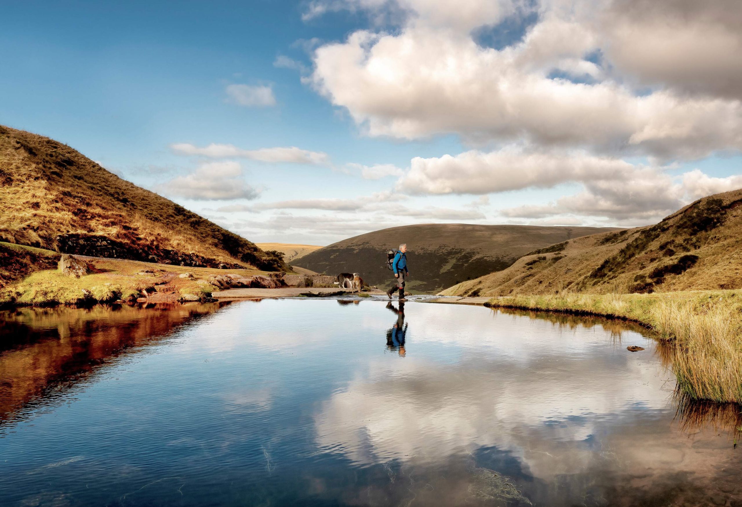 Level shot of a person hiking in front of body of water and surrounded by hills