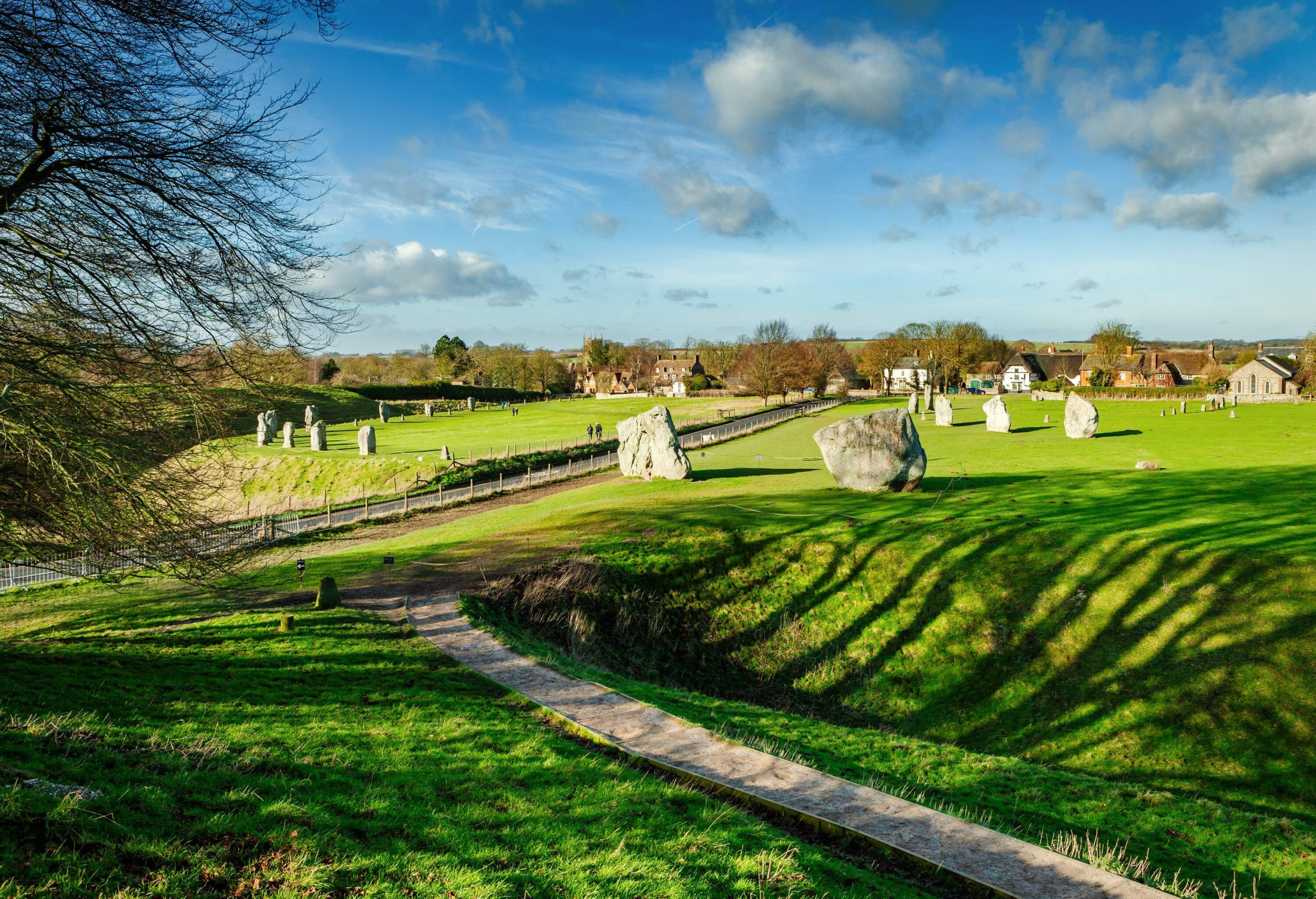 A wide-open field scattered with standing stones along a road, and a distant settlement.