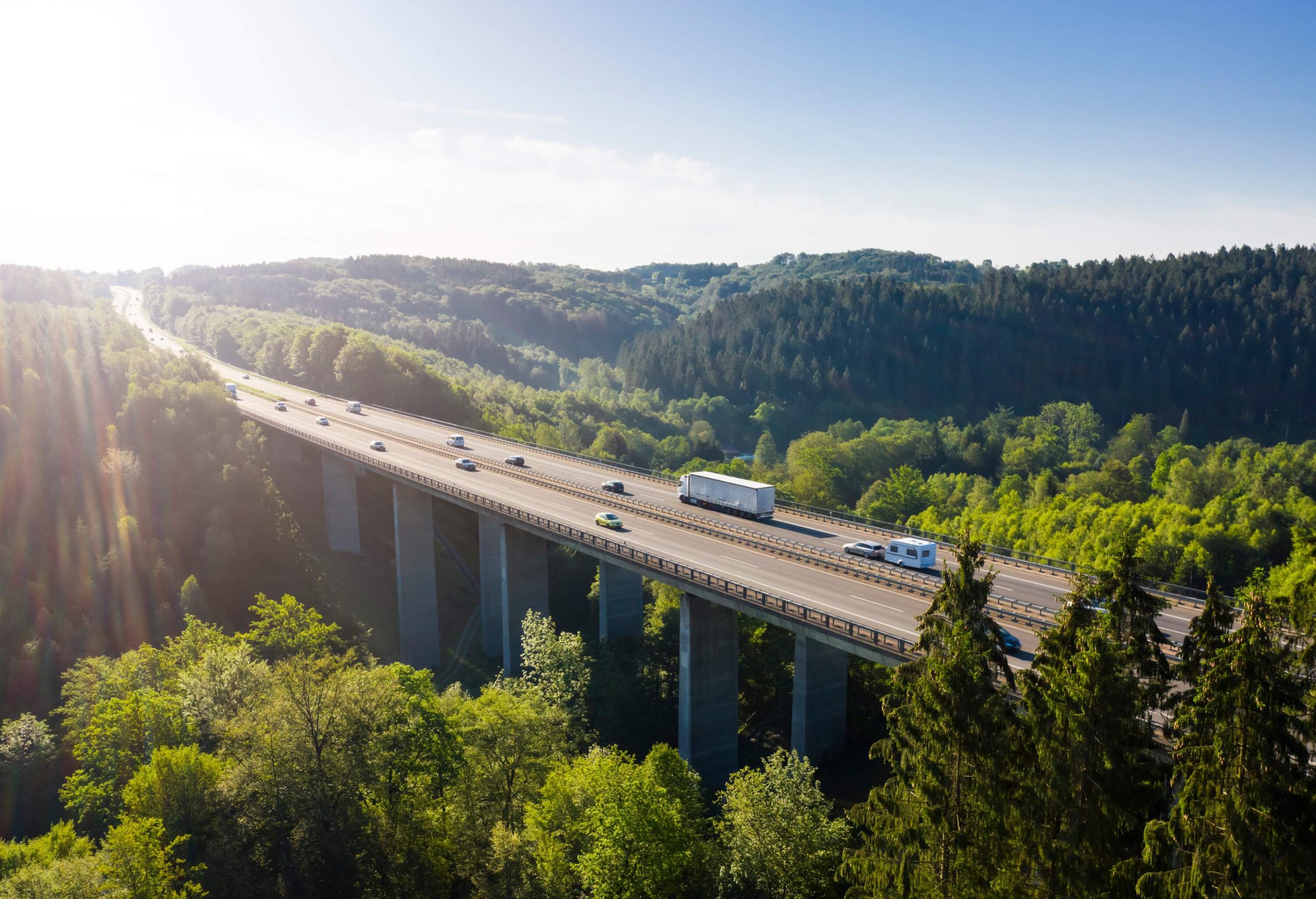 A massive concrete bridge across a valley covered in trees.