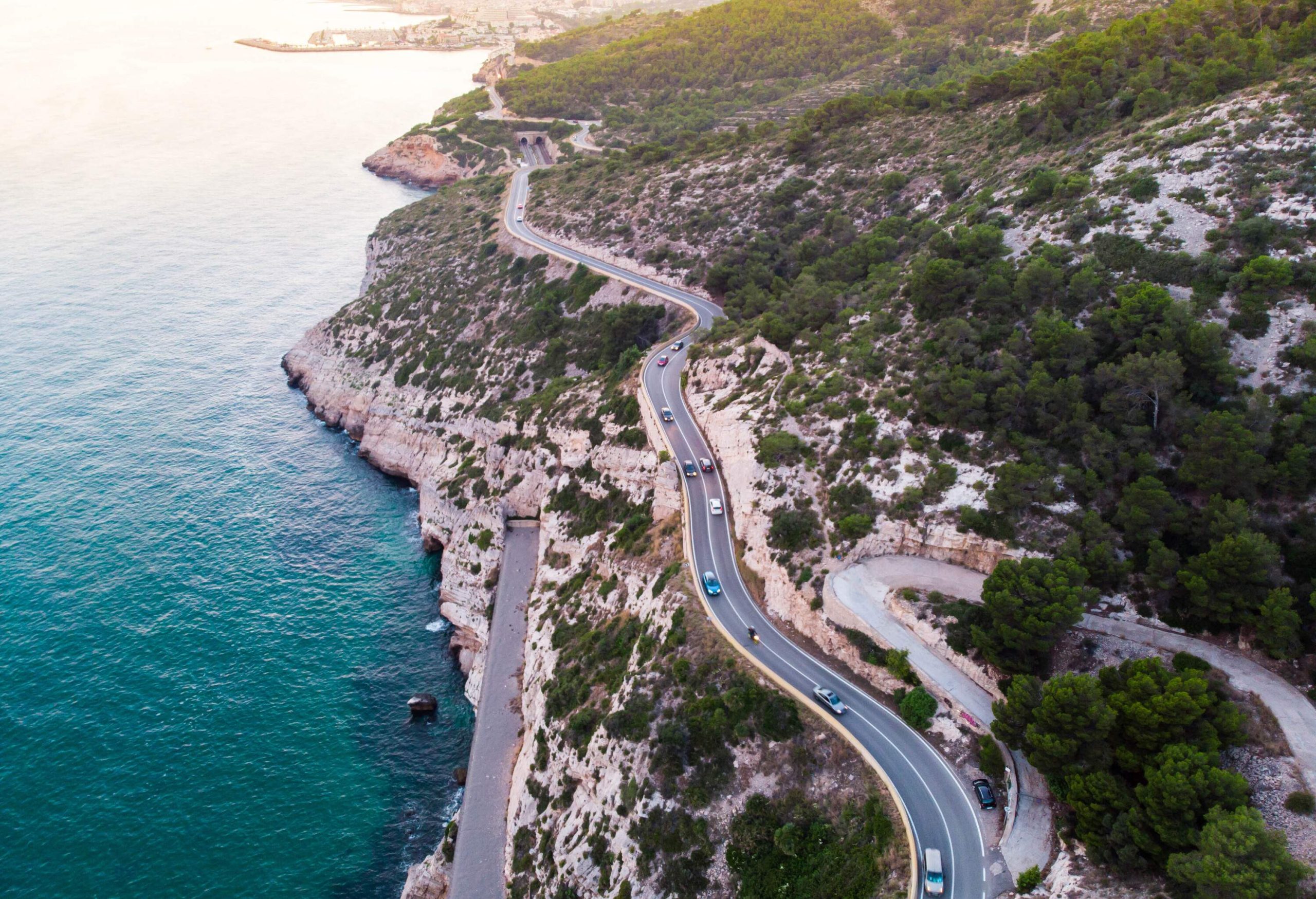 A roadway running along the sides of the mountains overlooking the blue ocean.