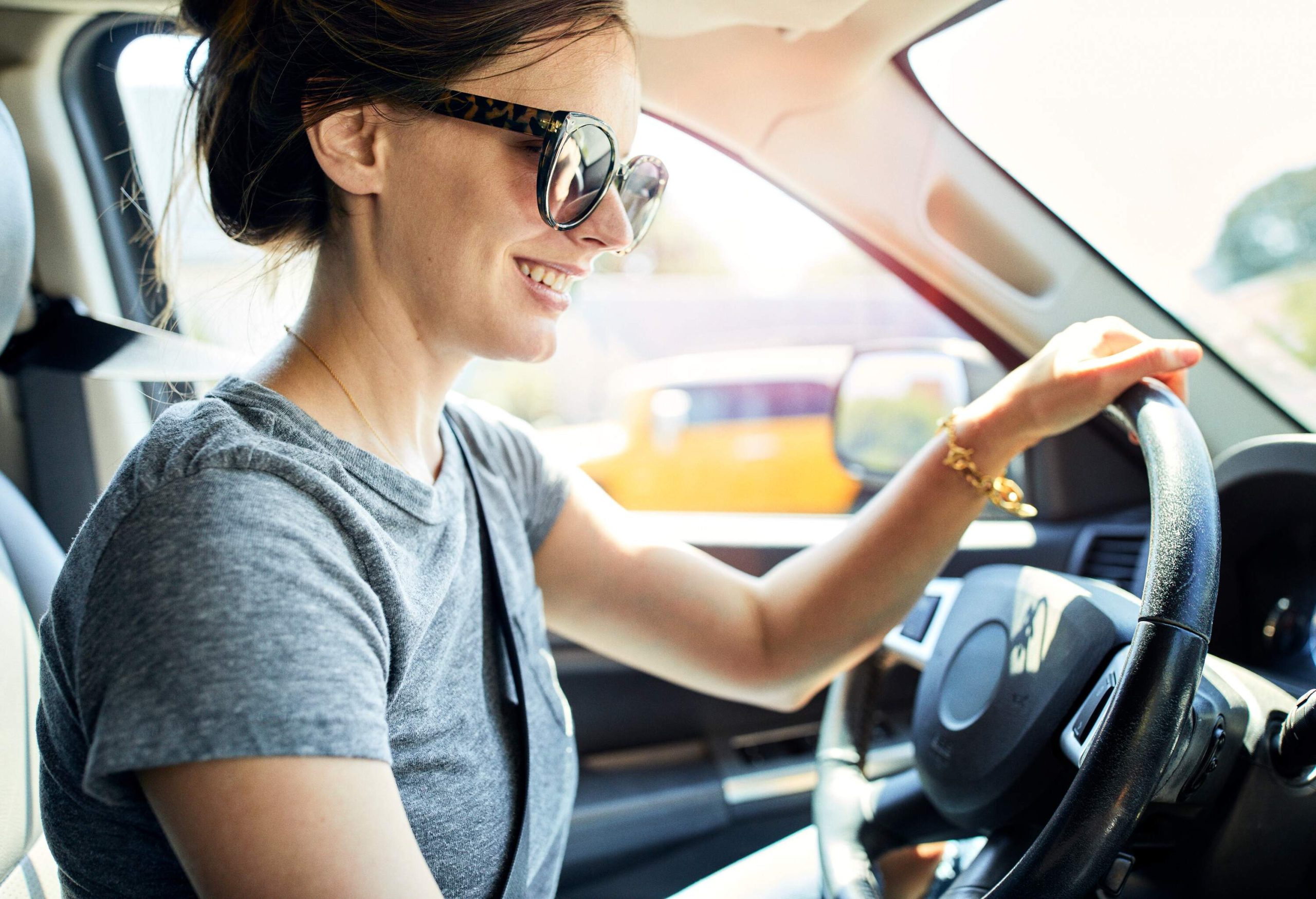 A happy female seated in the driver's seat of a car, ready to drive.