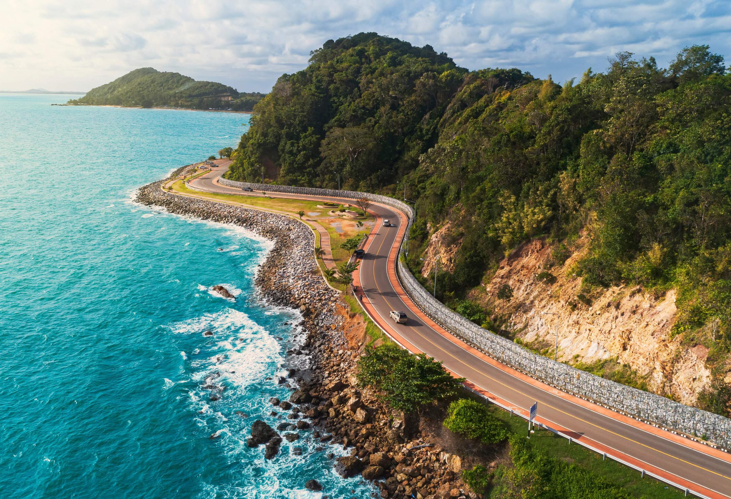 Cars travelling on a coastal road along the forested cliffs with vast ocean views.